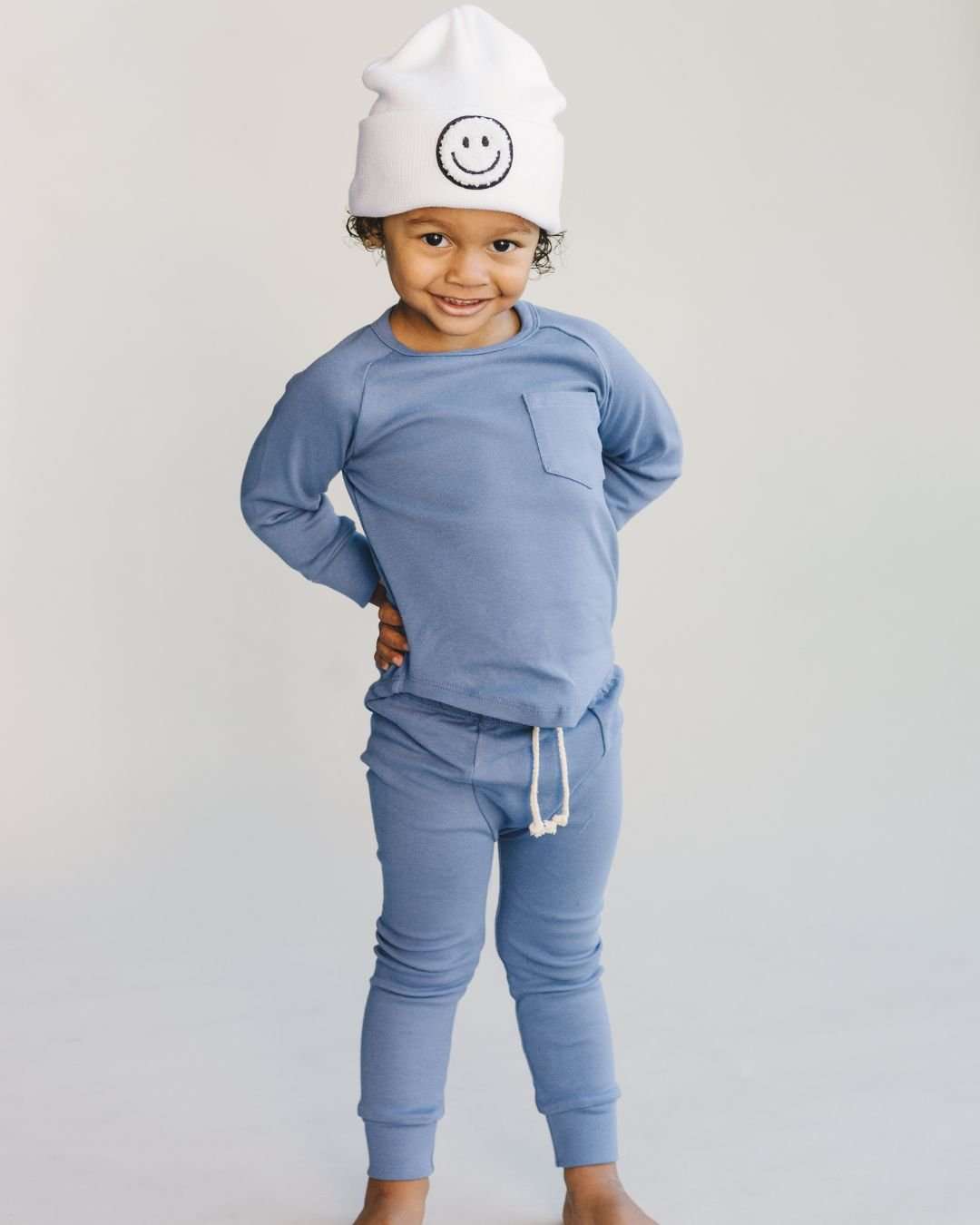 Child wearing lounge set ocean blue with smiley face beanie, featuring a cozy top and pants design.