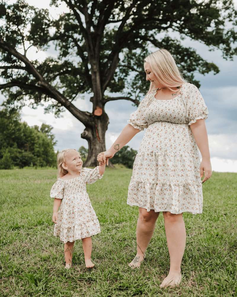 Mother and daughter wearing matching yellow floral dresses in a scenic outdoor setting.