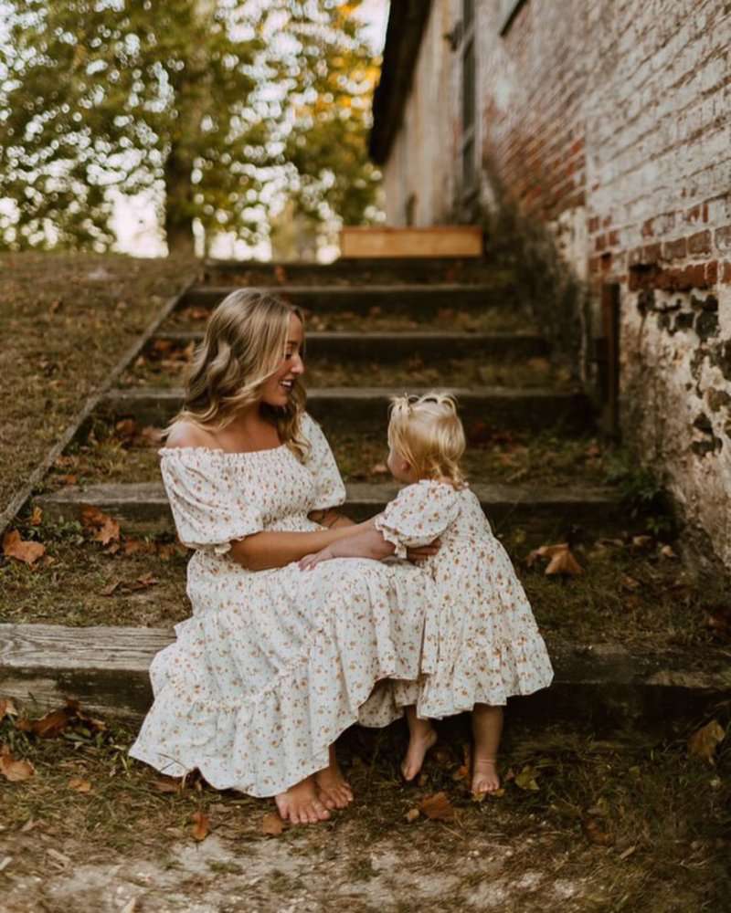 Mom and daughter in matching yellow floral dresses, enjoying a sunny day on outdoor stairs.