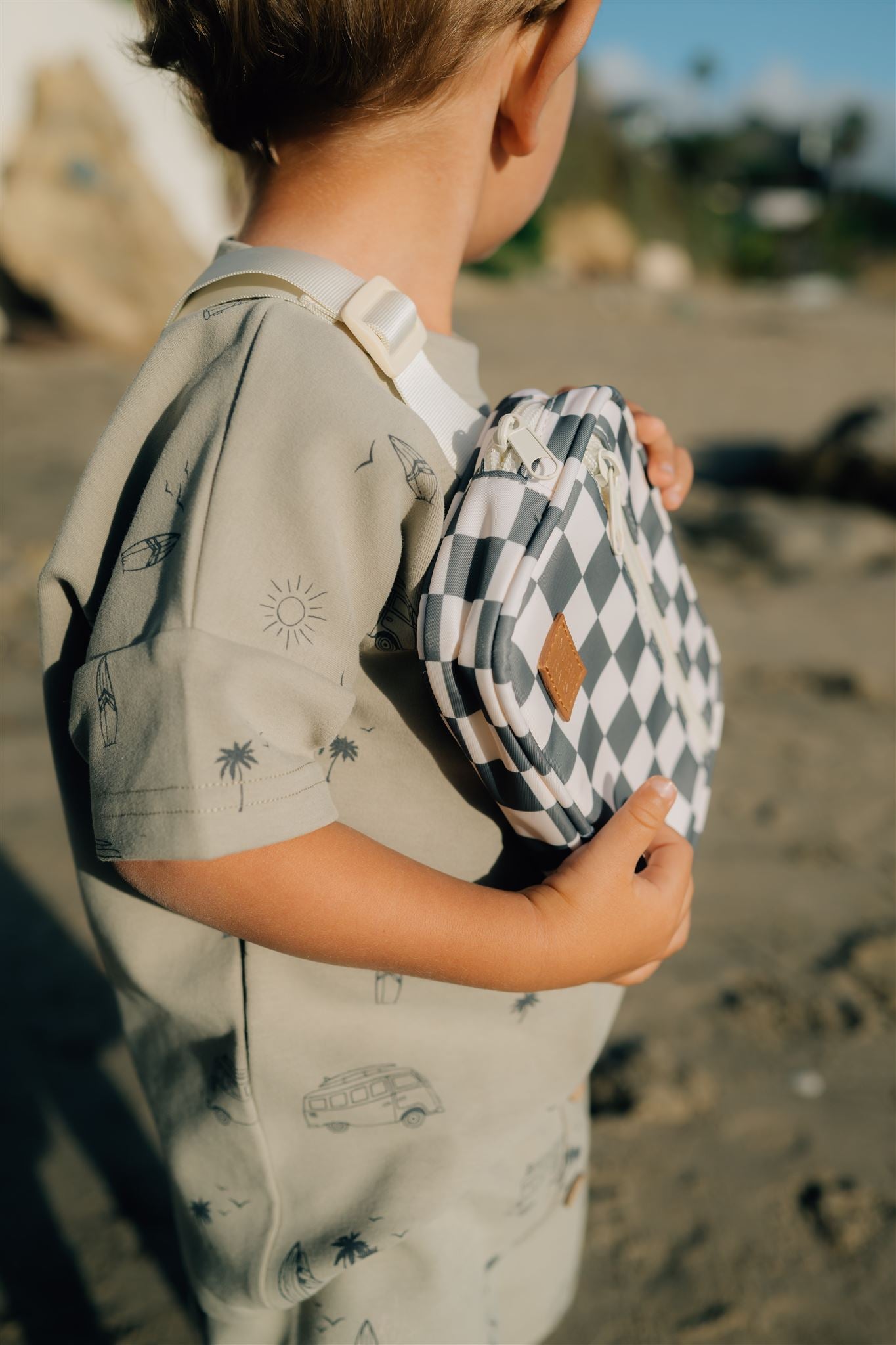 Child at the beach holding a green checkered mini fanny pack, showcasing a trendy and functional accessory.