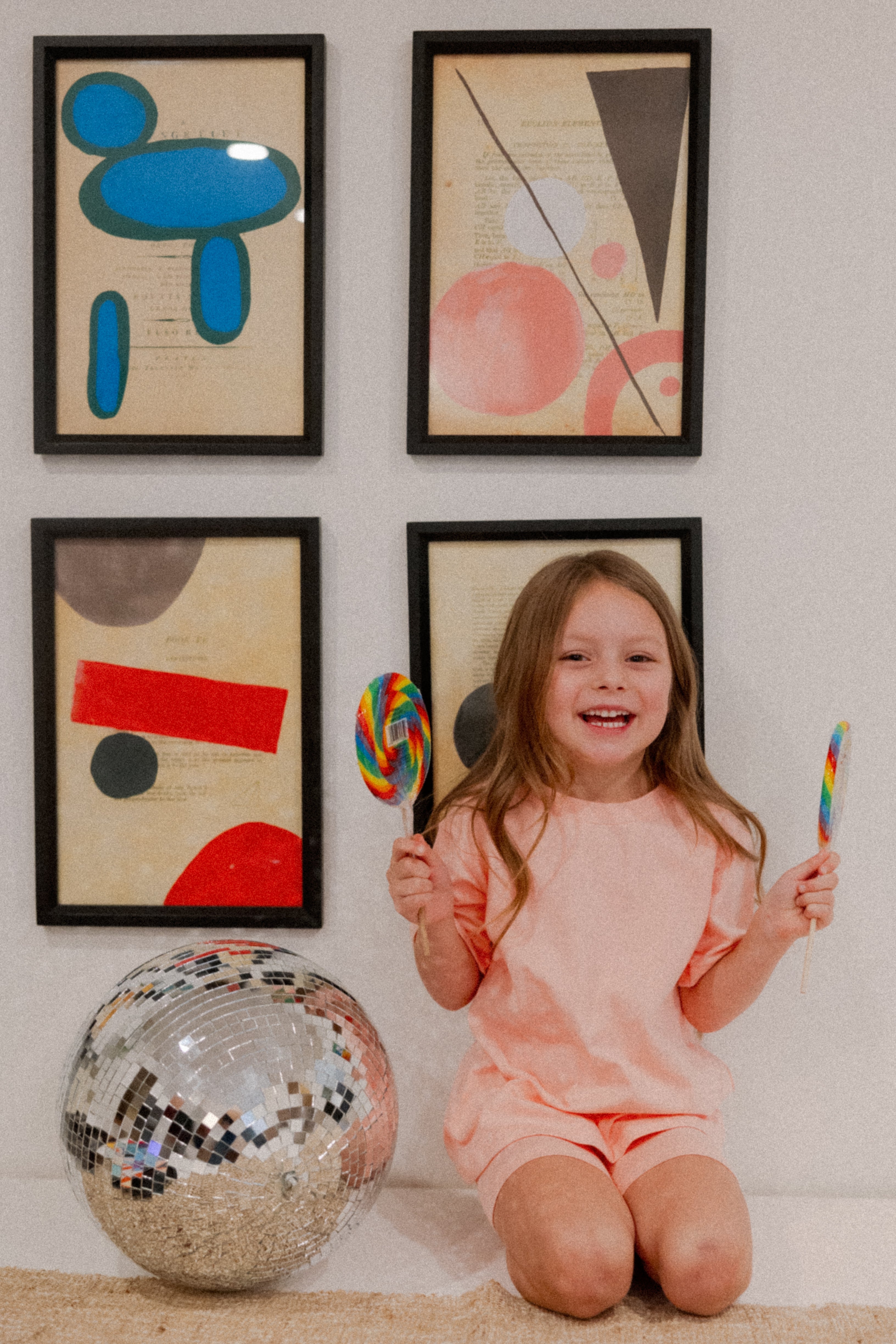 Child wearing the Indy Set in pink, holding lollipops, with colorful art and a disco ball in the background.