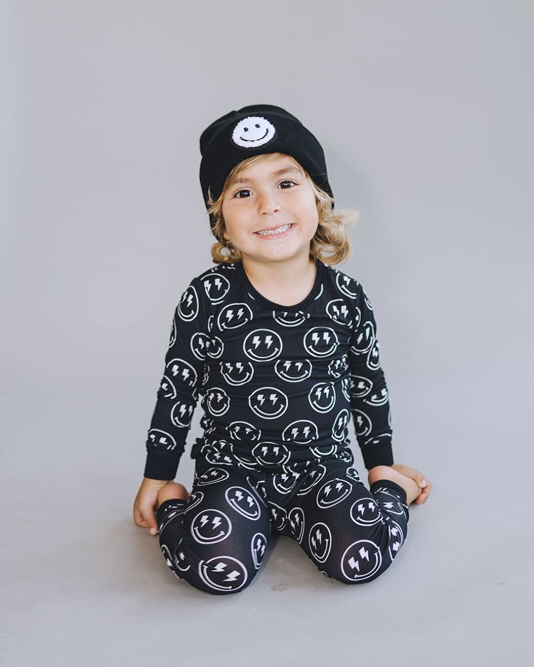 Child wearing a black Smiley Beanie and matching pajama set with smiley and lightning bolt patterns.