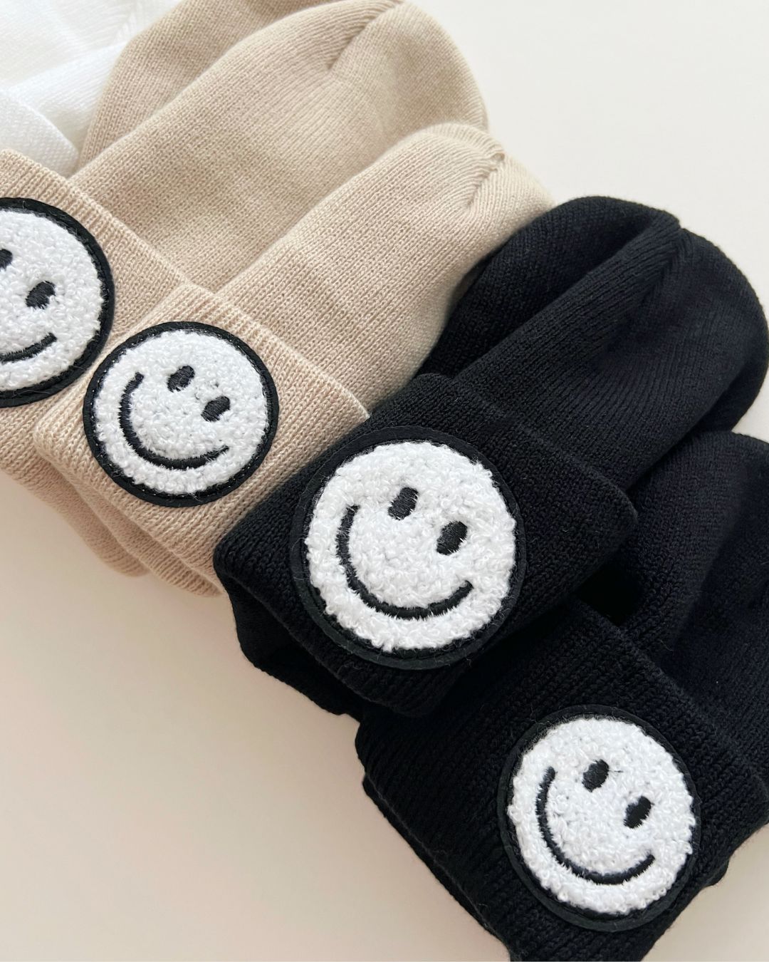 Smiley Beanie collection featuring black and beige colors with smiley face patches, perfect for cozy warmth.