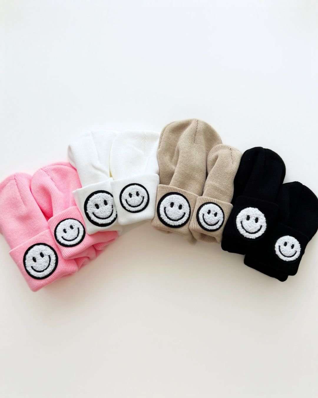 Colorful smiley beanies in pink, white, beige, and black, featuring cheerful smiley face patches.