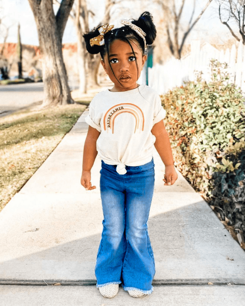 Toddler girl wearing Sophie Denim Bell Bottoms and a rainbow shirt, showcasing stylish casual attire outdoors.