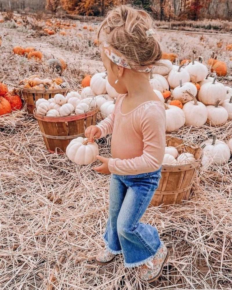 Toddler girl in bell bottom jeans picking a pumpkin in a pumpkin patch during autumn.
