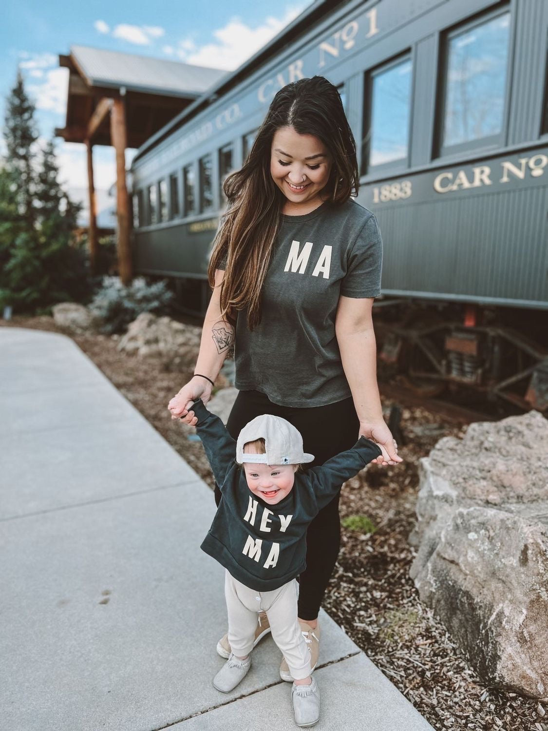 Mom and child wearing matching Hey Ma kids sweatshirt and adult tee, showcasing playful, stylish family outfits.