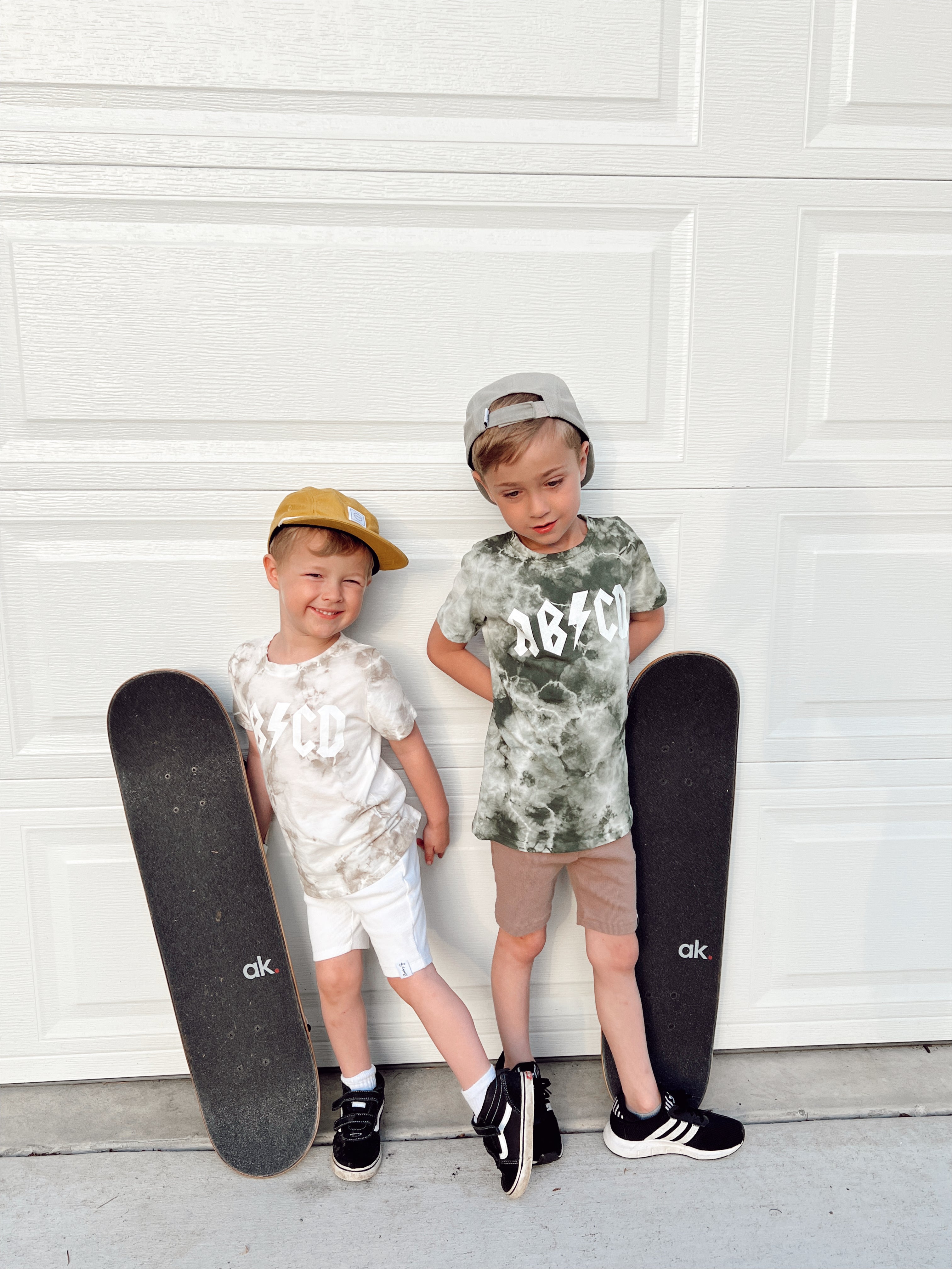 Two boys wearing ABCD Tie Dye Tees holding skateboards in front of a garage door.