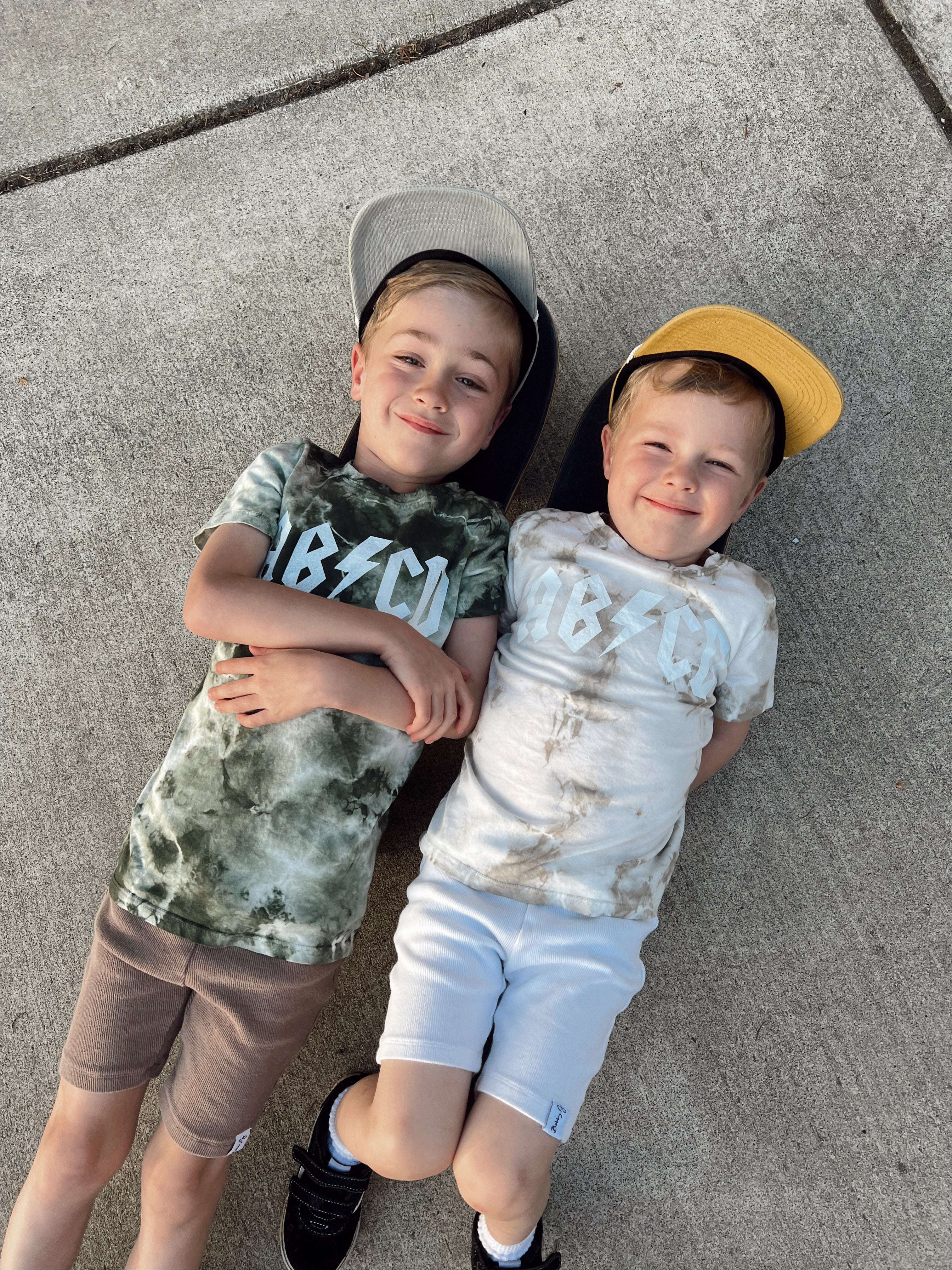Two kids lying on the ground wearing ABCD Tie Dye Tees in playful colors, showcasing comfort and style.