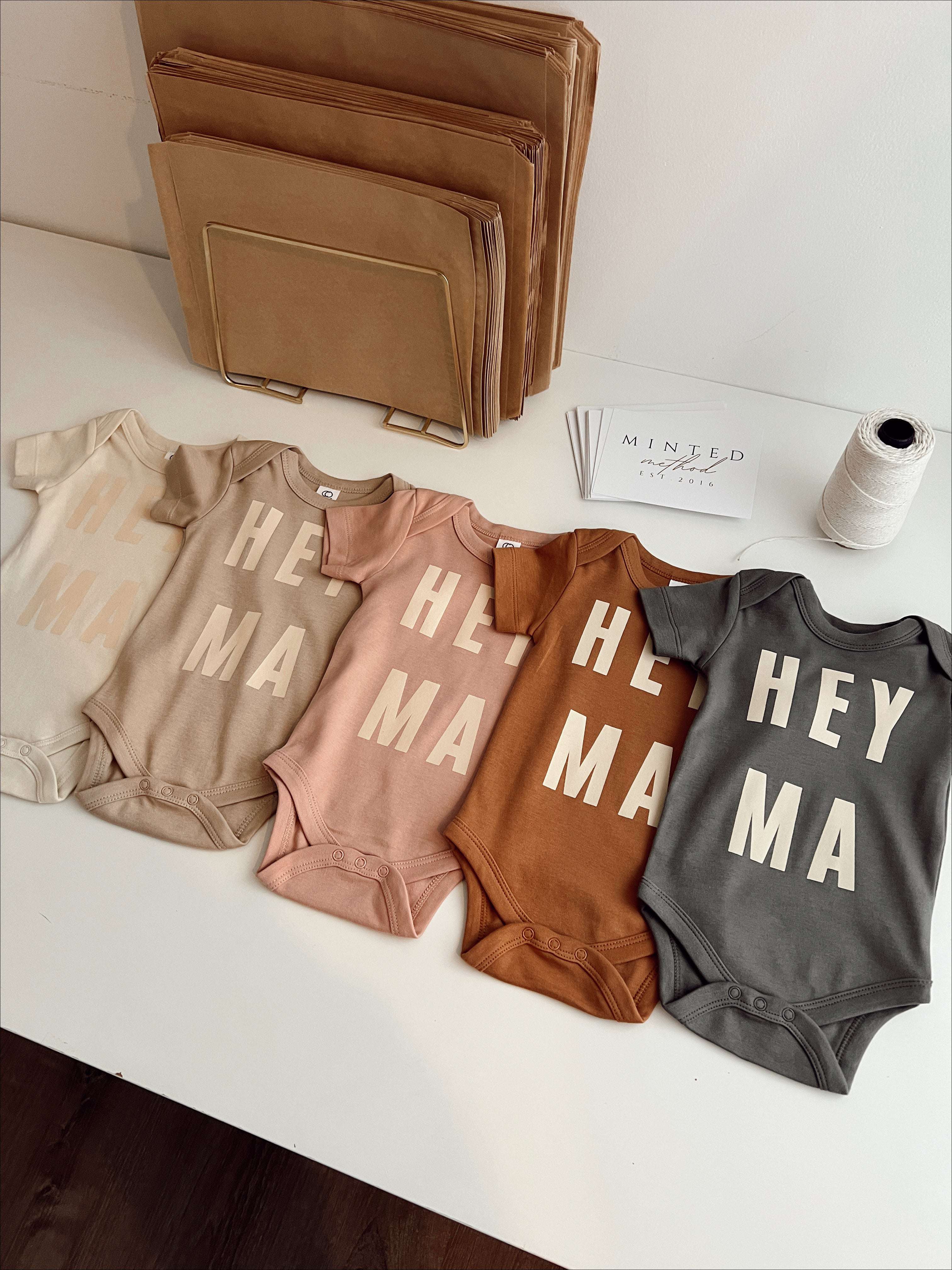 Selection of Hey Ma organic baby onesies in various colors, showcasing trendy, ethically made baby clothes.