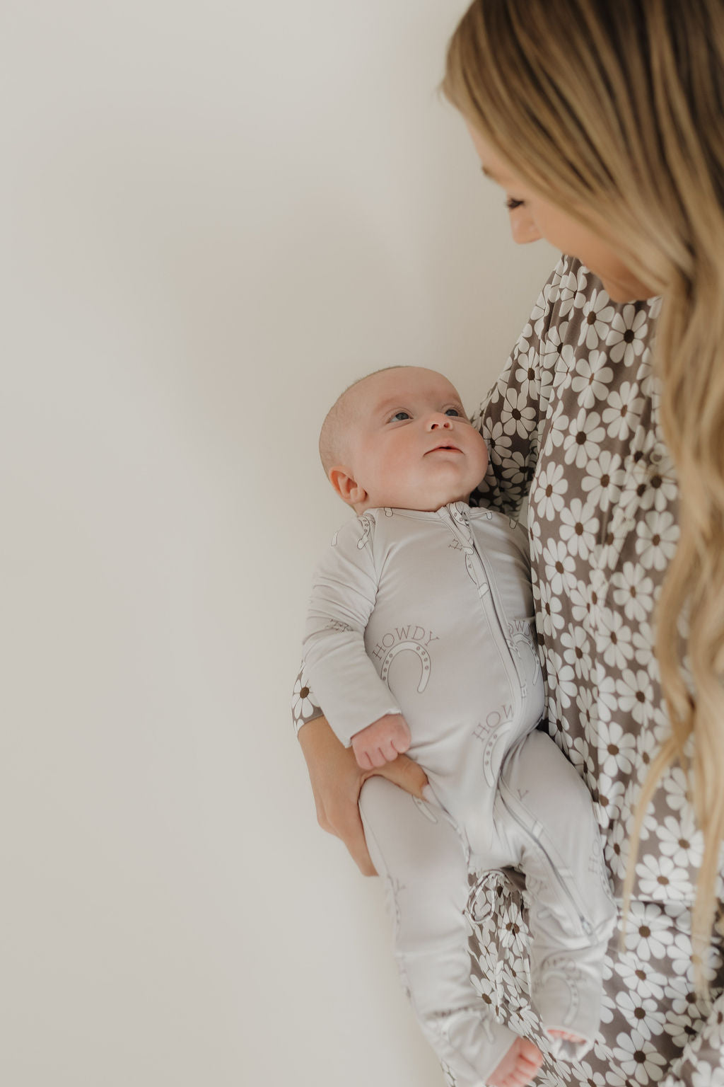 Mother holding a baby in a cozy outfit, showcasing a nurturing moment with a floral pajama backdrop.