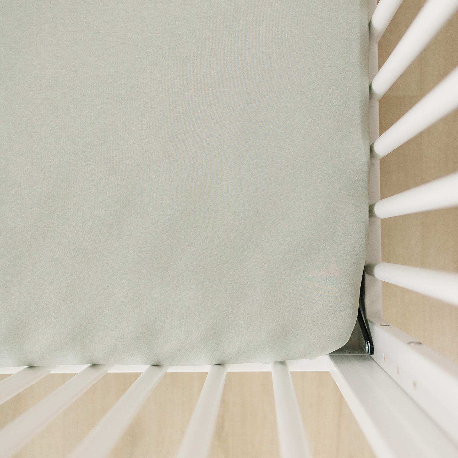 Bamboo crib sheet sage fitted on a standard crib mattress with white slats.