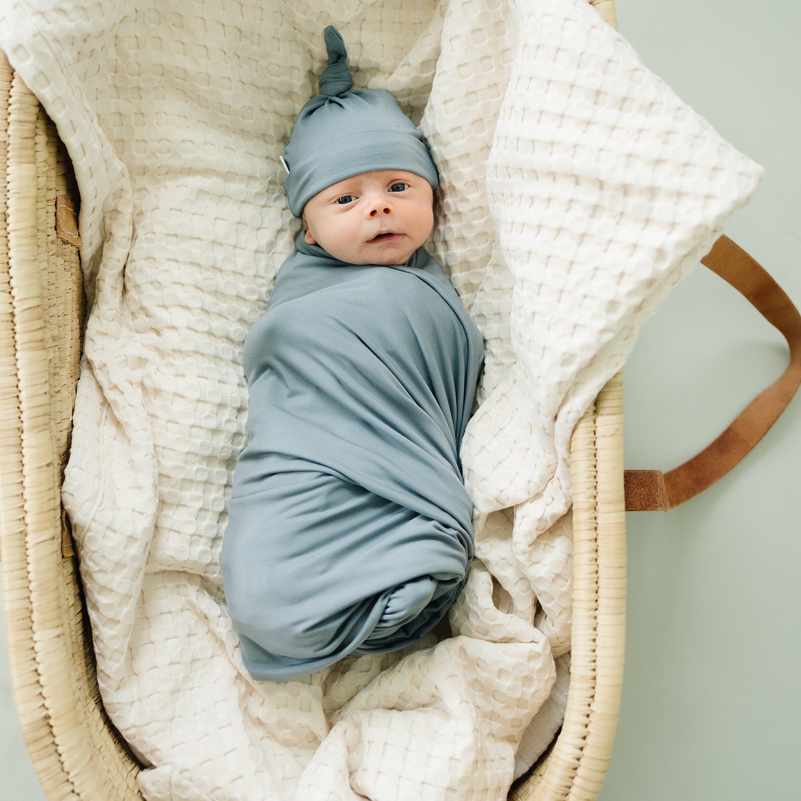 Bamboo Stretch Swaddle Dusty Blue used for wrapping a newborn in a cozy basket, highlighting softness and comfort.