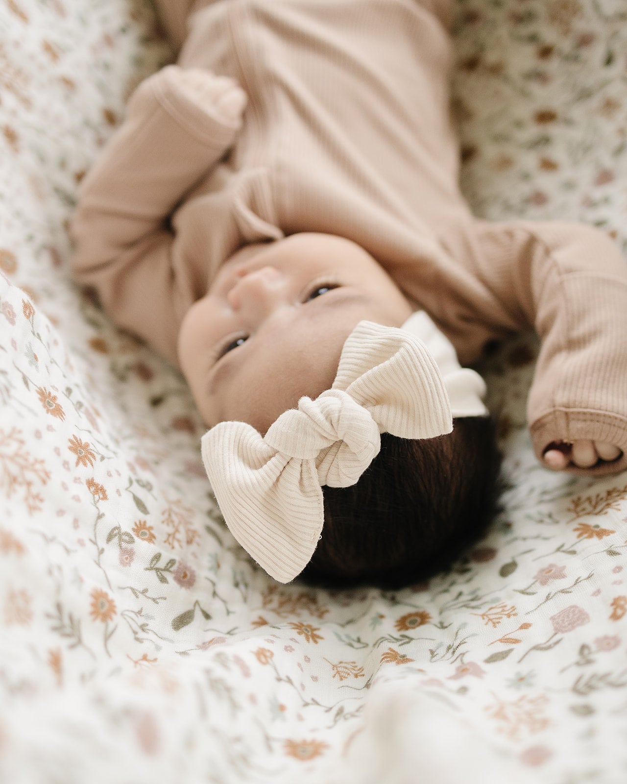 Infant wearing a vanilla organic baby head wrap, resting on a floral blanket.