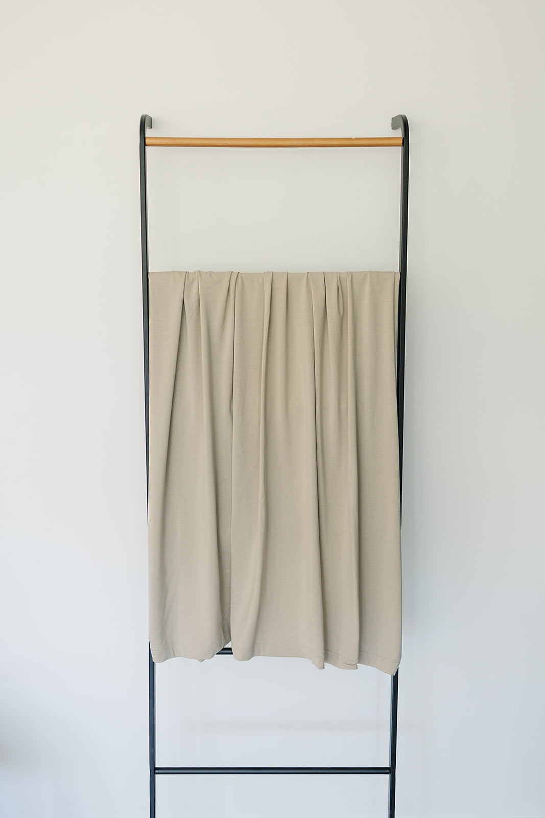 Bamboo Stretch Swaddle Oatmeal displayed on a minimalist rack, highlighting its neutral color and soft fabric.