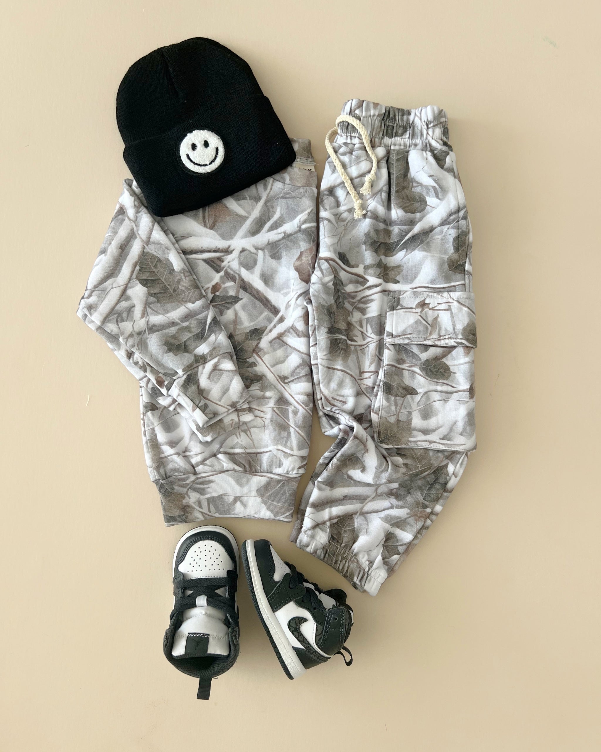 Camo kids lounge set featuring a pullover hoodie, cargo joggers, beanie, and sneakers on a neutral background.