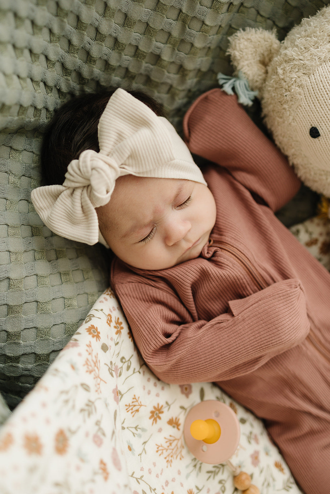 Baby wearing a vanilla organic cotton ribbed head wrap, peacefully sleeping in a cozy setting with a stuffed animal.