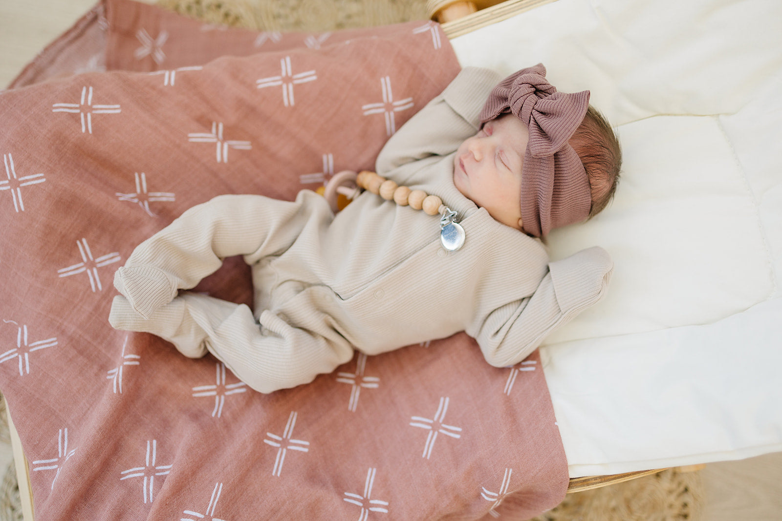 Baby peacefully sleeping on a soft Muslin Swaddle Blanket with a modern peach print, wearing a cozy outfit and headband.