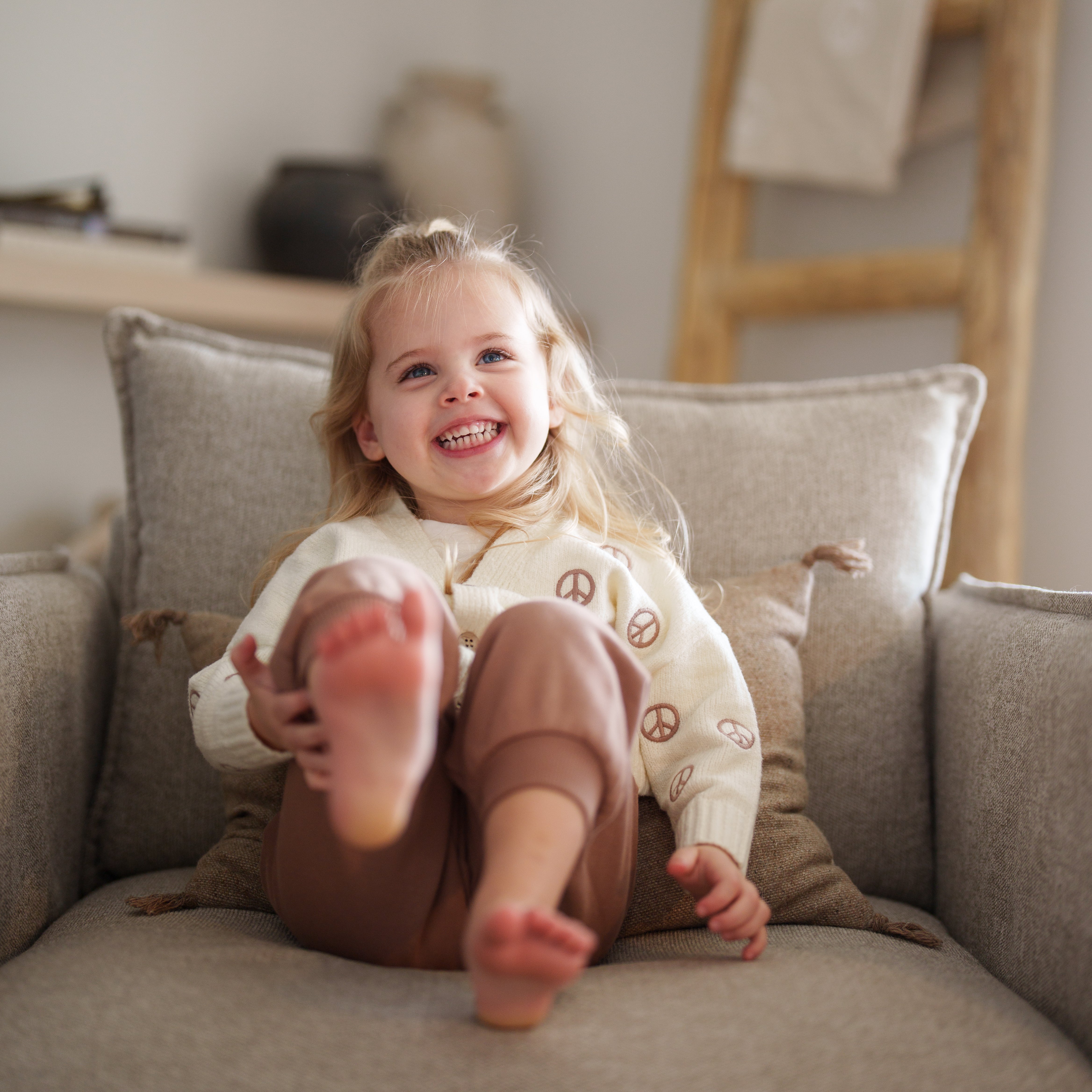 Oversized Sweatpant - Cozy Neutral Bottoms for Babies & Kids worn by a smiling child sitting on a couch.