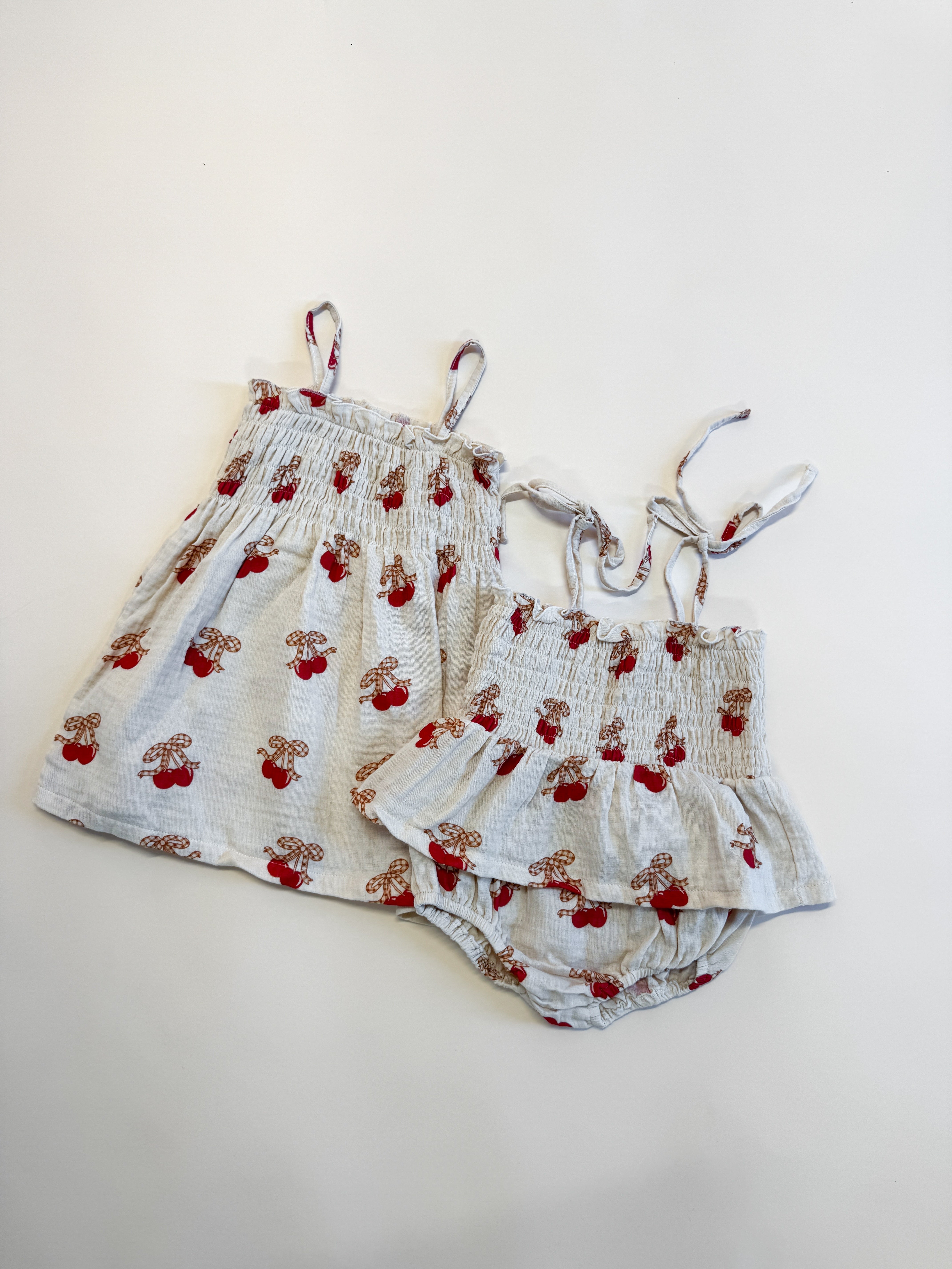 Printed smocked dress and matching bloomers with cherry print on soft background, perfect for little ones.