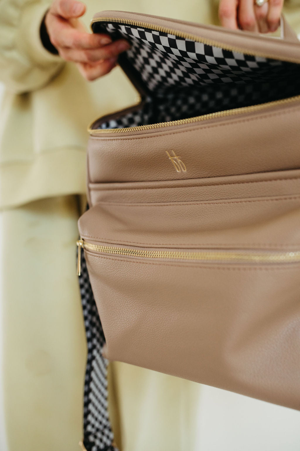 Open ff diaper bag taupe showcasing black checkerboard interior and multiple compartments for organization.