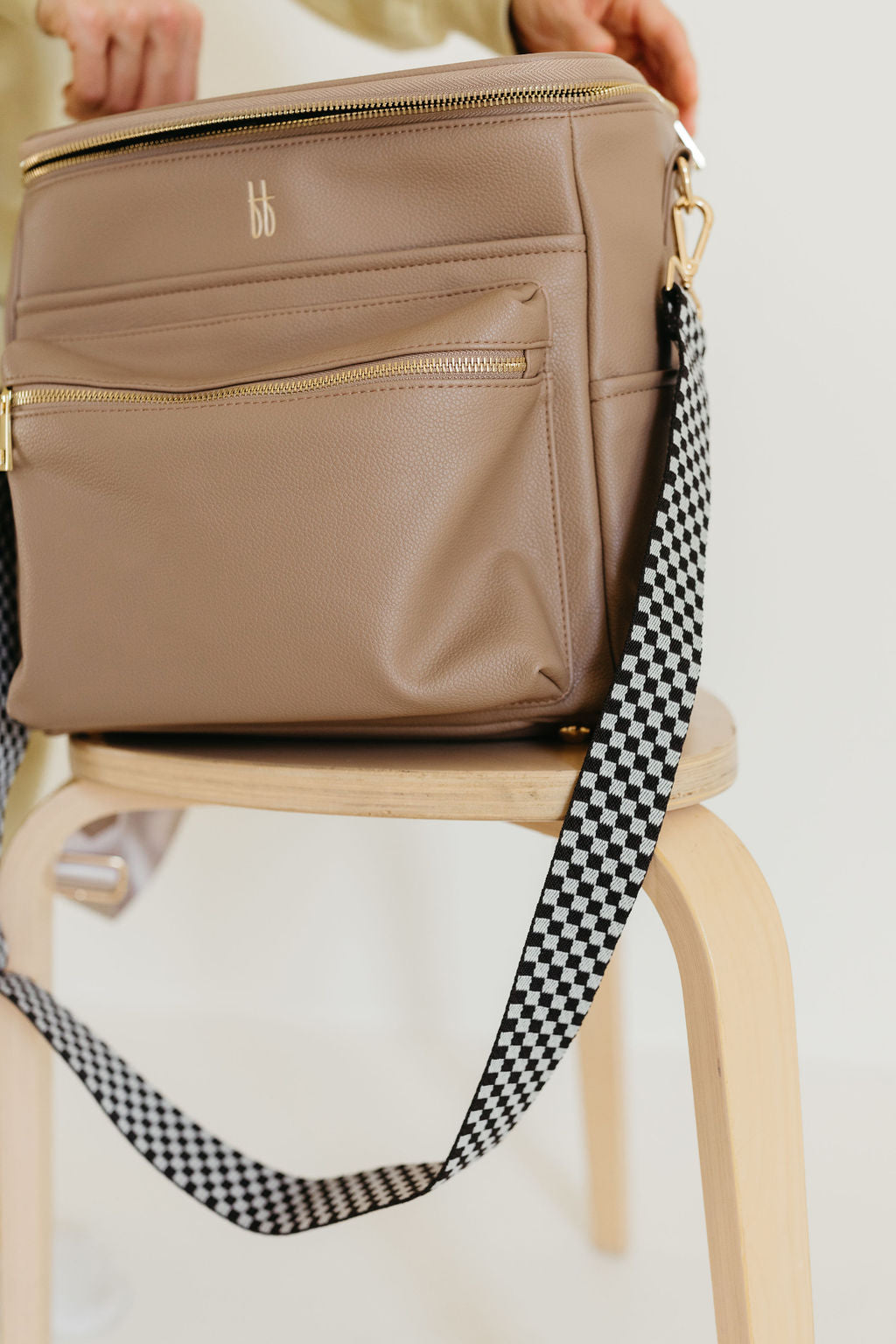 ff diaper bag taupe with black checkered strap on a wooden chair, showcasing its stylish design and functionality.