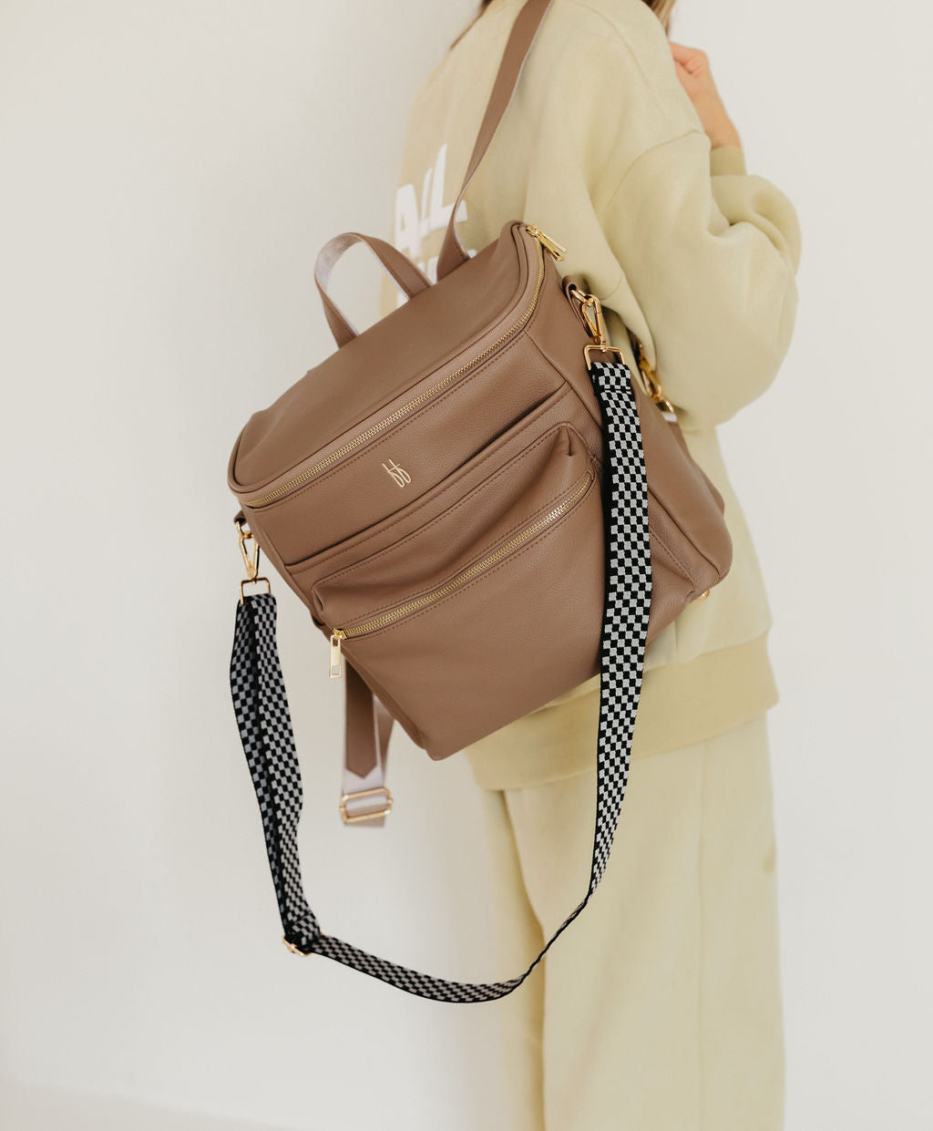 Stylish ff diaper bag taupe made of vegan leather, featuring a black checkerboard strap, perfect for everyday use.