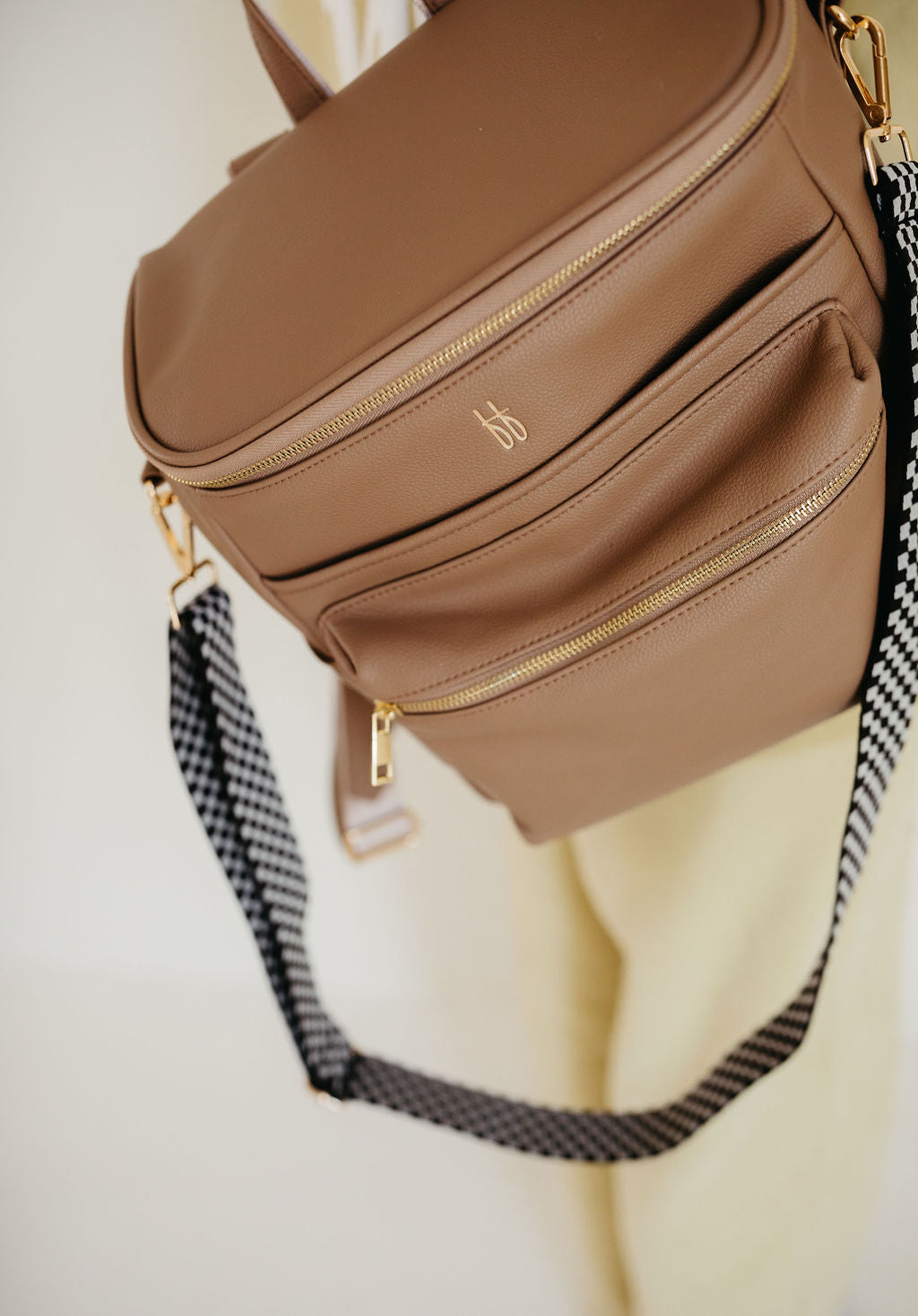 ff diaper bag taupe in vegan leather showing dual zip pockets and a black checkerboard strap.