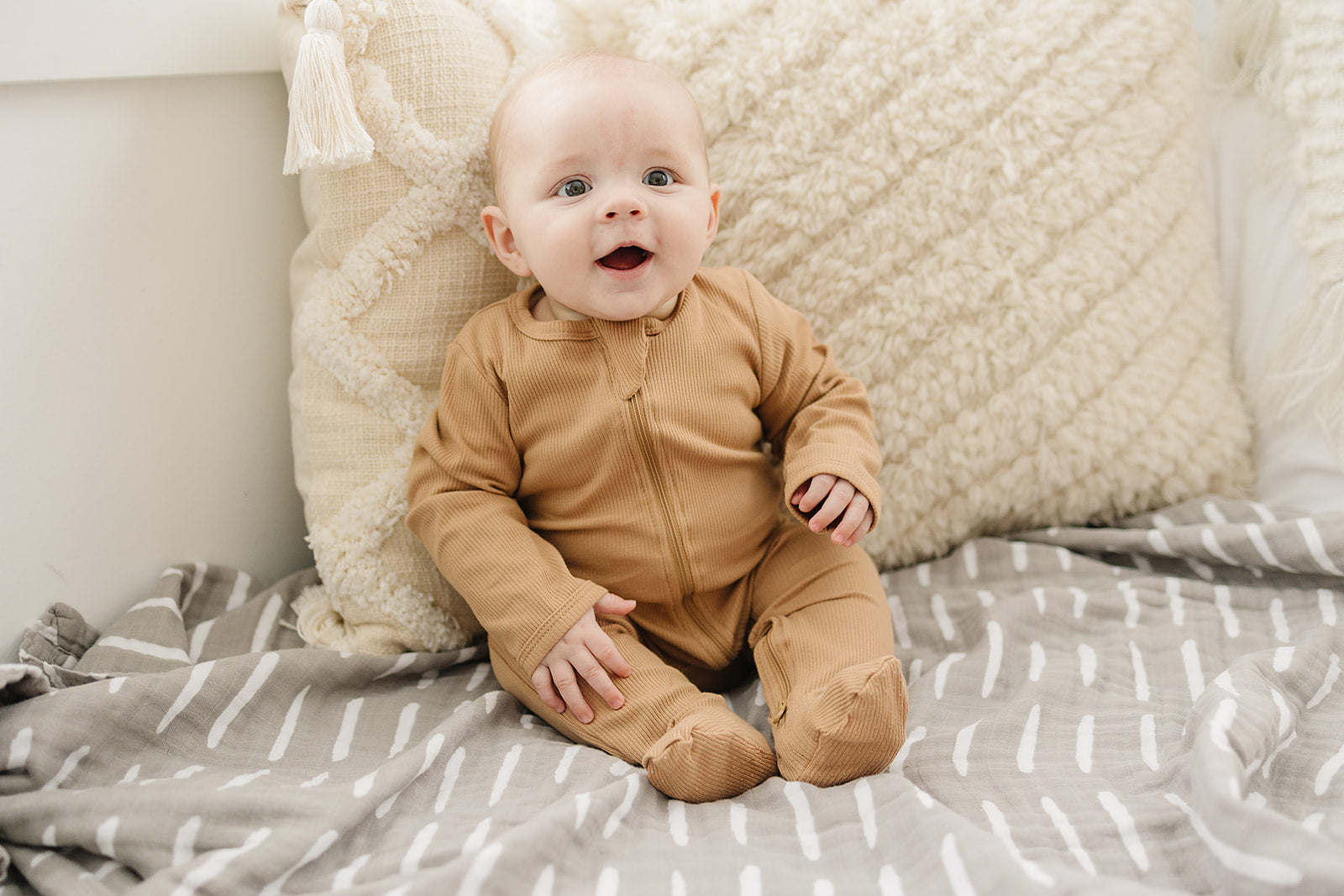 Baby wearing cozy cafe organic cotton ribbed zipper pajamas sitting on a soft blanket.