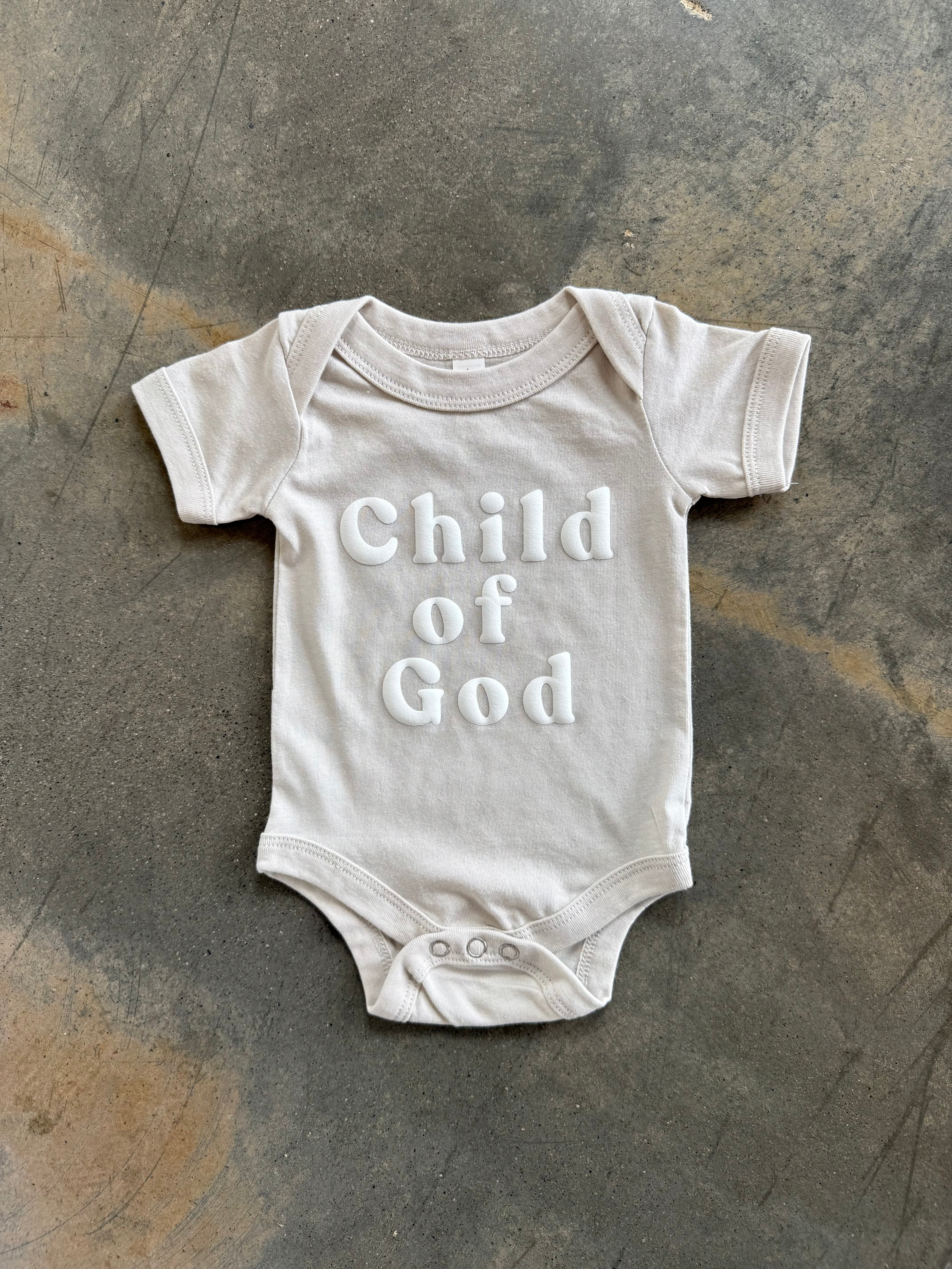 Child of God Onesie laying on concrete floor