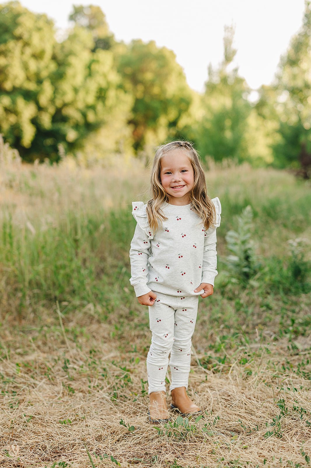 Girl in cherry ruffle French terry set playing outdoors, featuring ruffle sleeves and cherry-print leggings.
