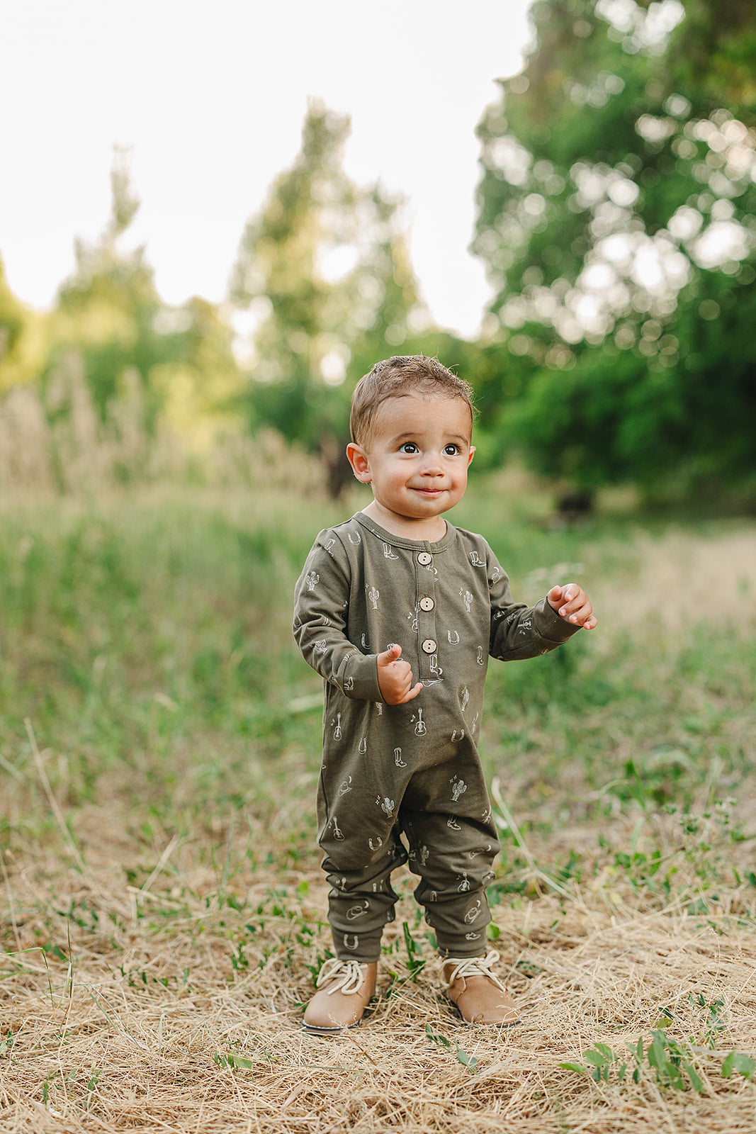 Adorable baby wearing a Nashville long sleeve button romper in a field, showcasing its cozy and cute design.