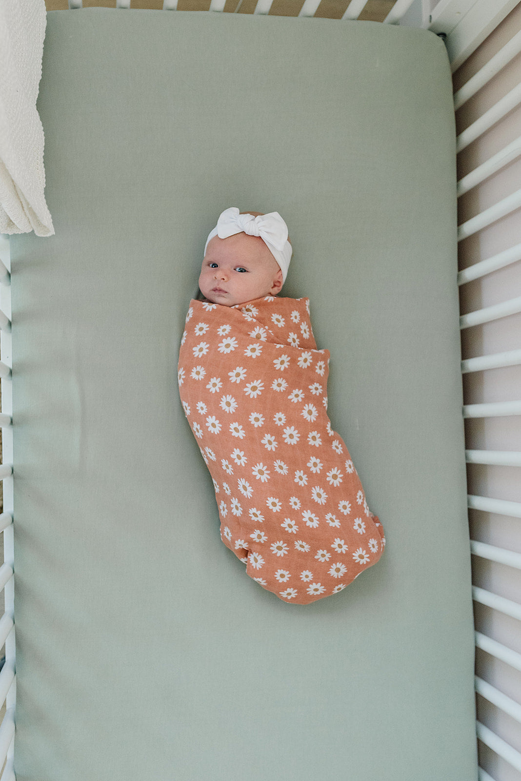 Baby swaddled in floral blanket on bamboo crib sheet sage, promoting comfort and style in nursery.