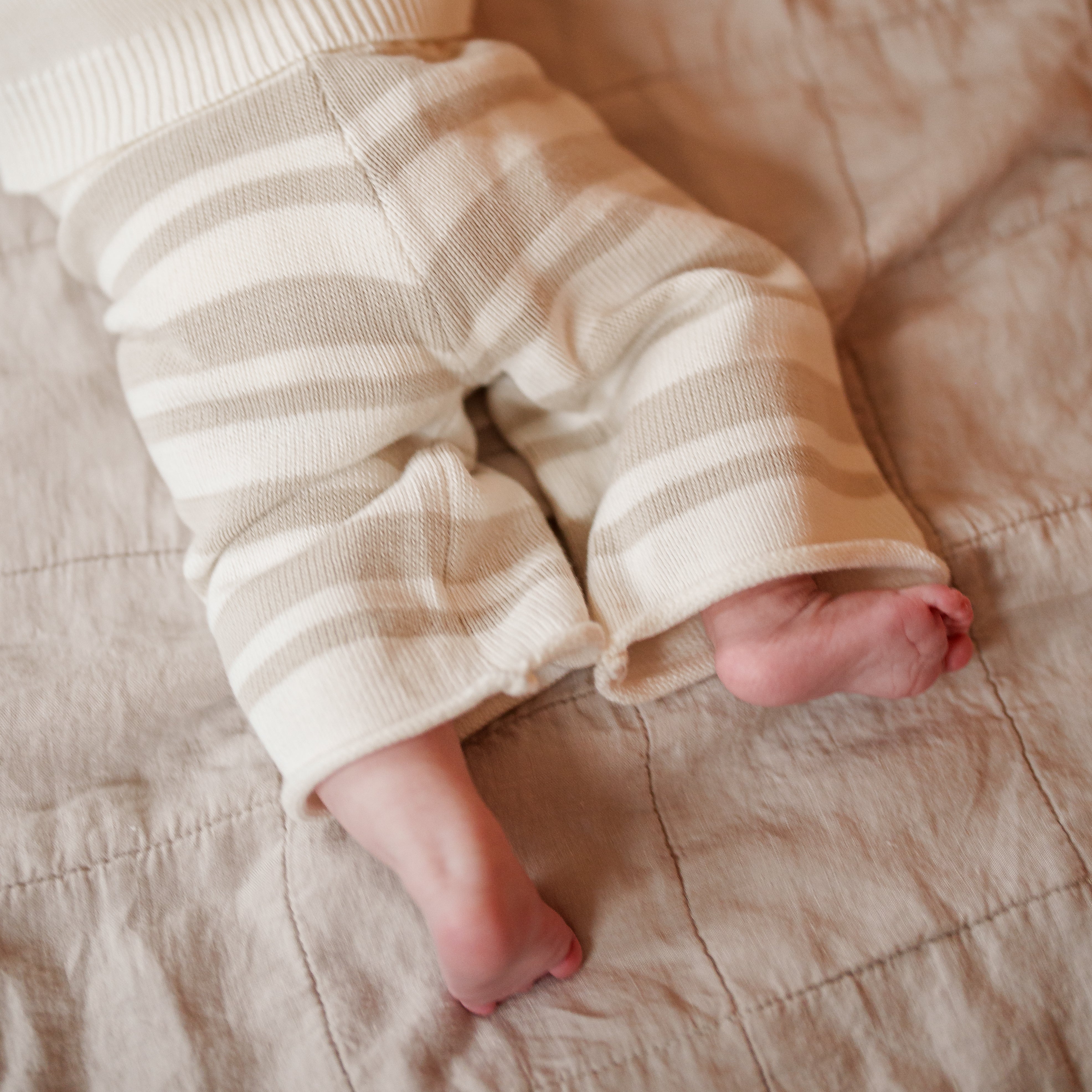 Close-up of baby legs in Organic Knit Wideleg Pant with beige and cream stripes on a soft blanket.