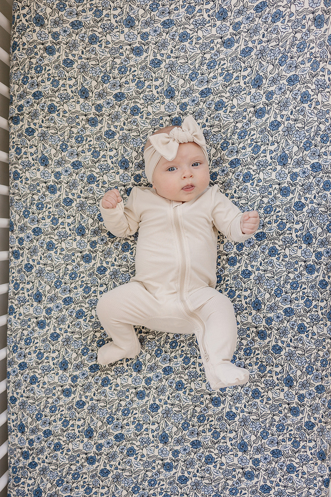 Baby lying on Bluebell Pointelle bamboo crib sheet with blue floral pattern and cream outfit.