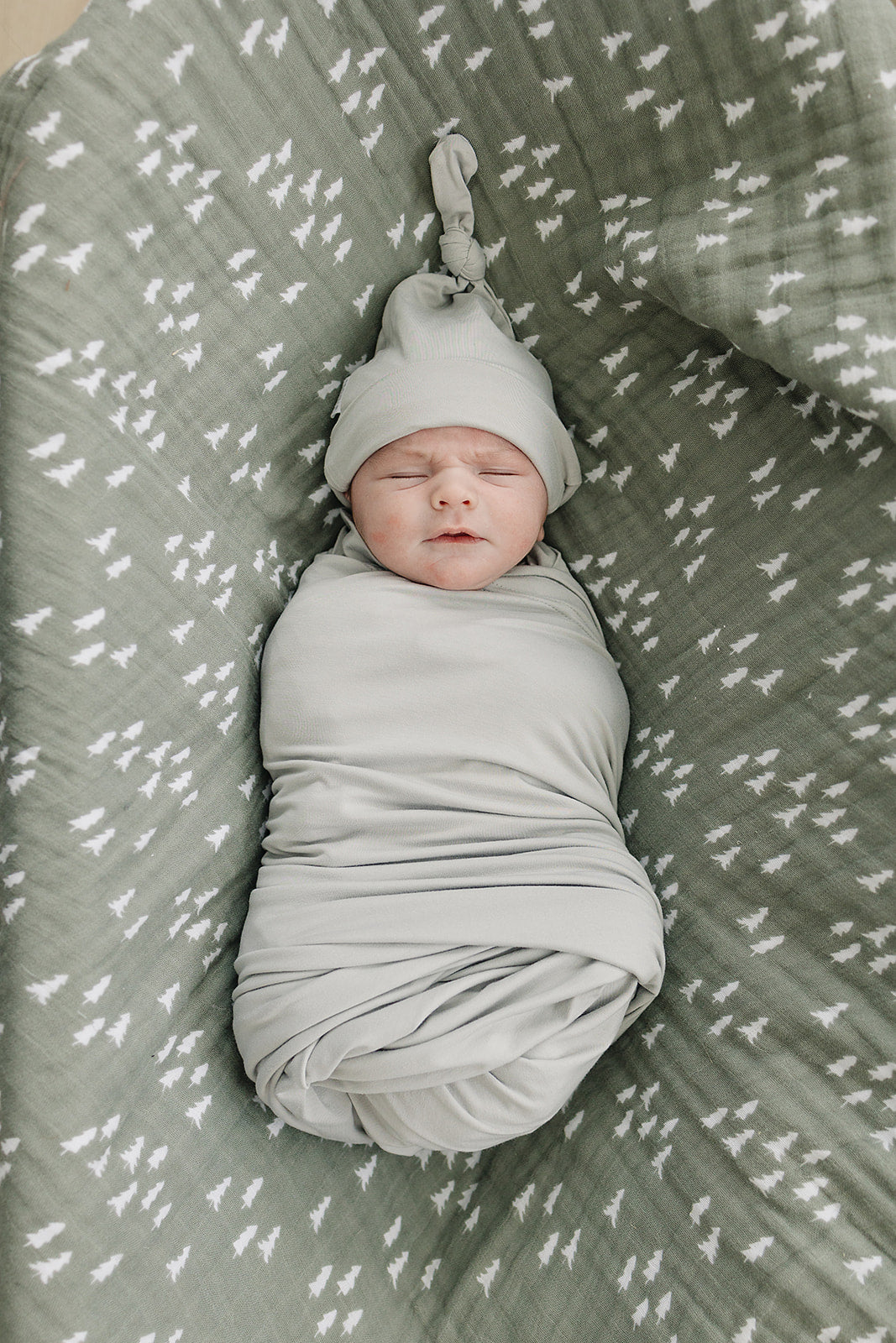Bamboo Stretch Swaddle Sage - Baby wrap swaddling a newborn with a cozy sage blanket and hat.