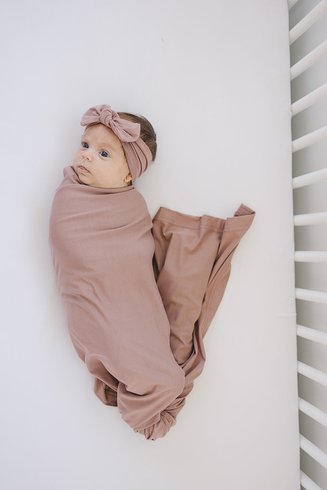 Bamboo Stretch Swaddle Dusty Rose wrapped around a baby, showcasing soft fabric and a stylish headband.