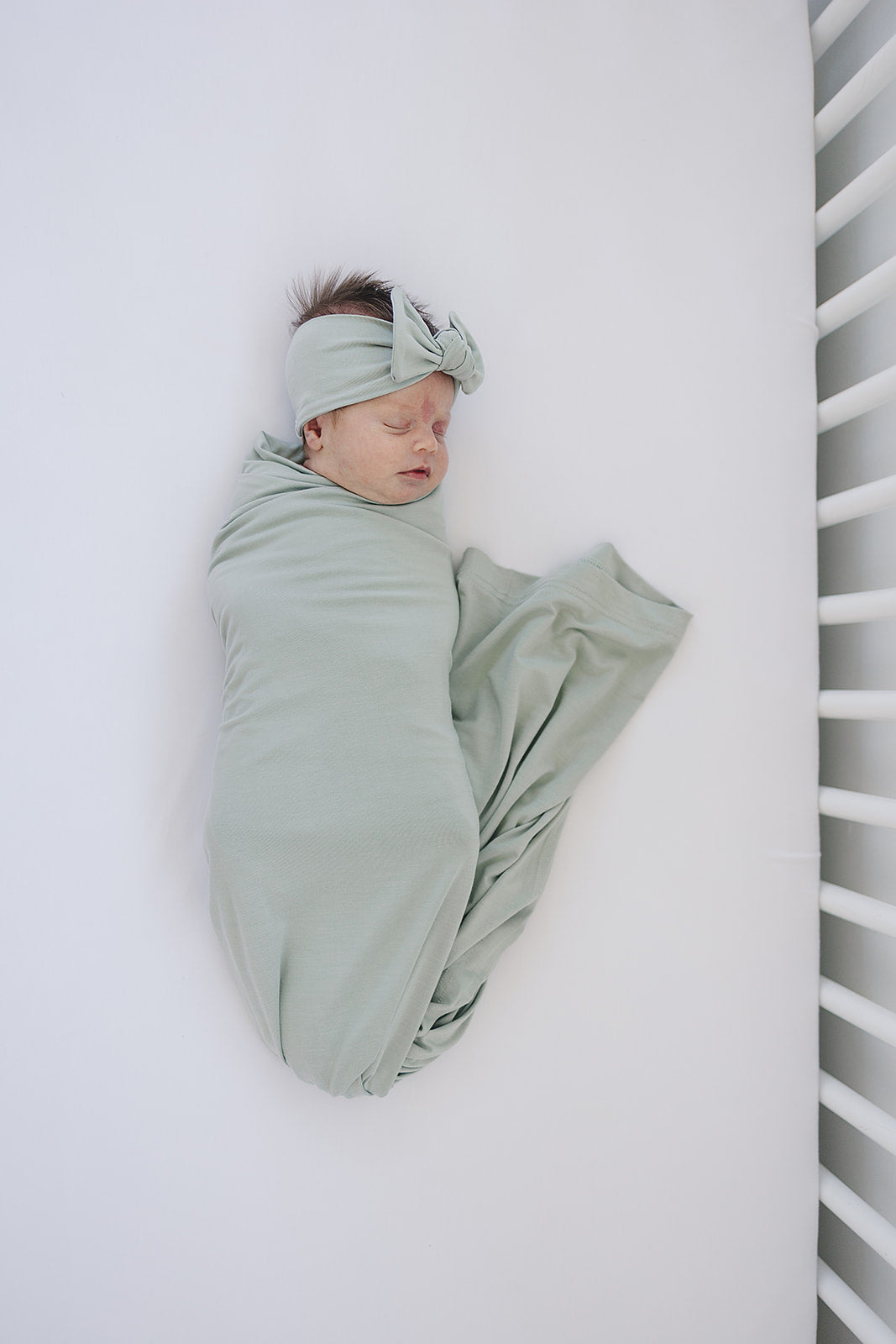 Bamboo Stretch Swaddle Sage - Baby wrap, cozy newborn wrapped in a soft sage swaddle laying in a crib.