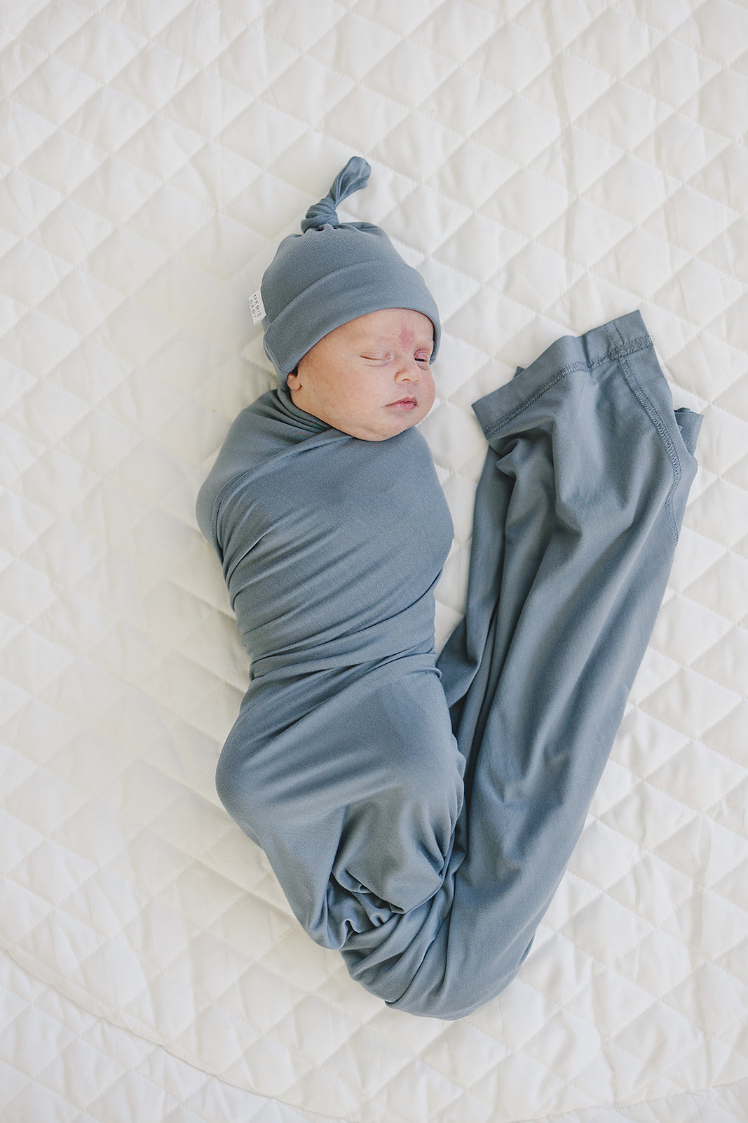 Bamboo Stretch Swaddle Dusty Blue gently wraps a newborn, providing comfort and elegance in a soft bamboo fabric.