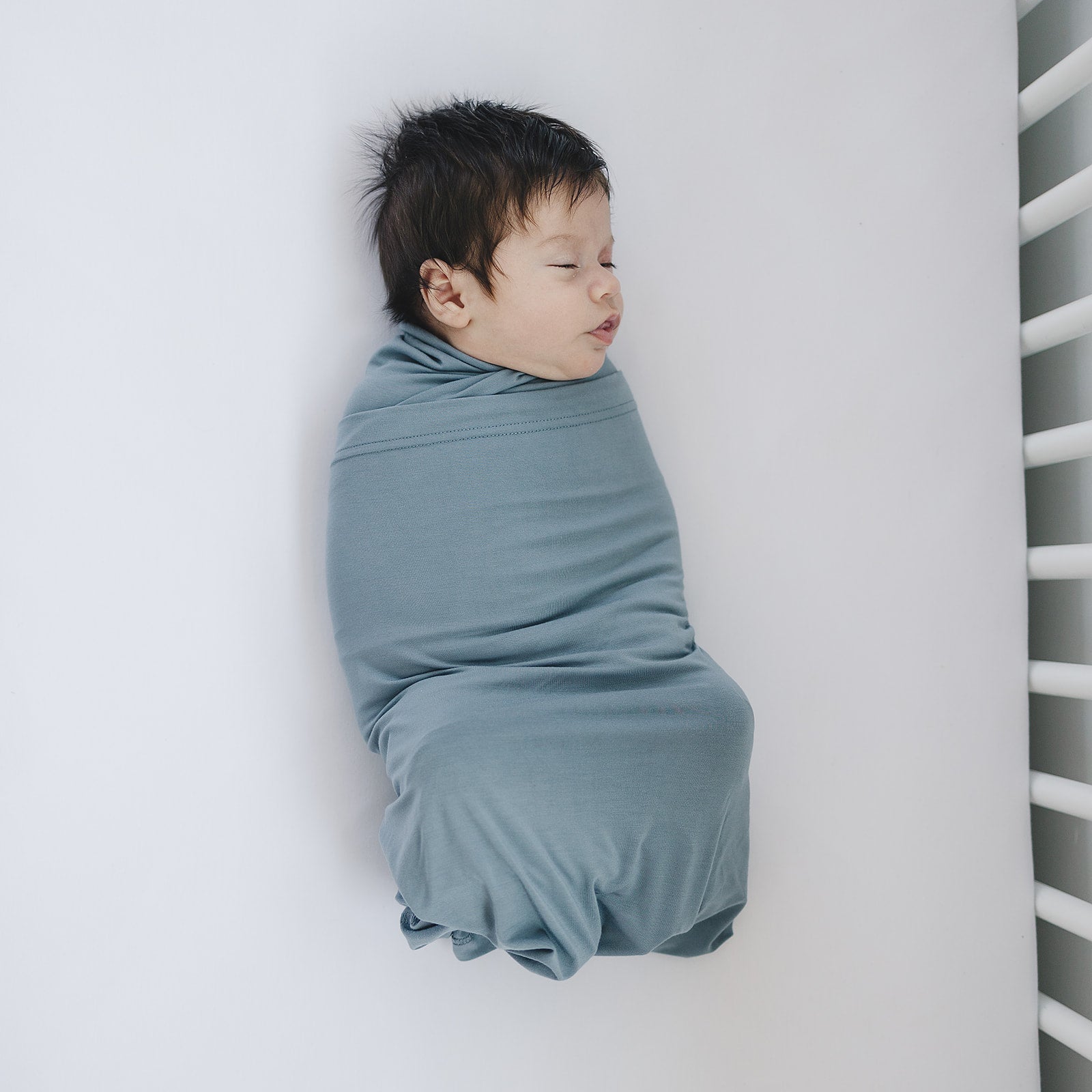 Baby wrapped in Bamboo Stretch Swaddle Dusty Blue, showcasing its soft fabric and cozy design.