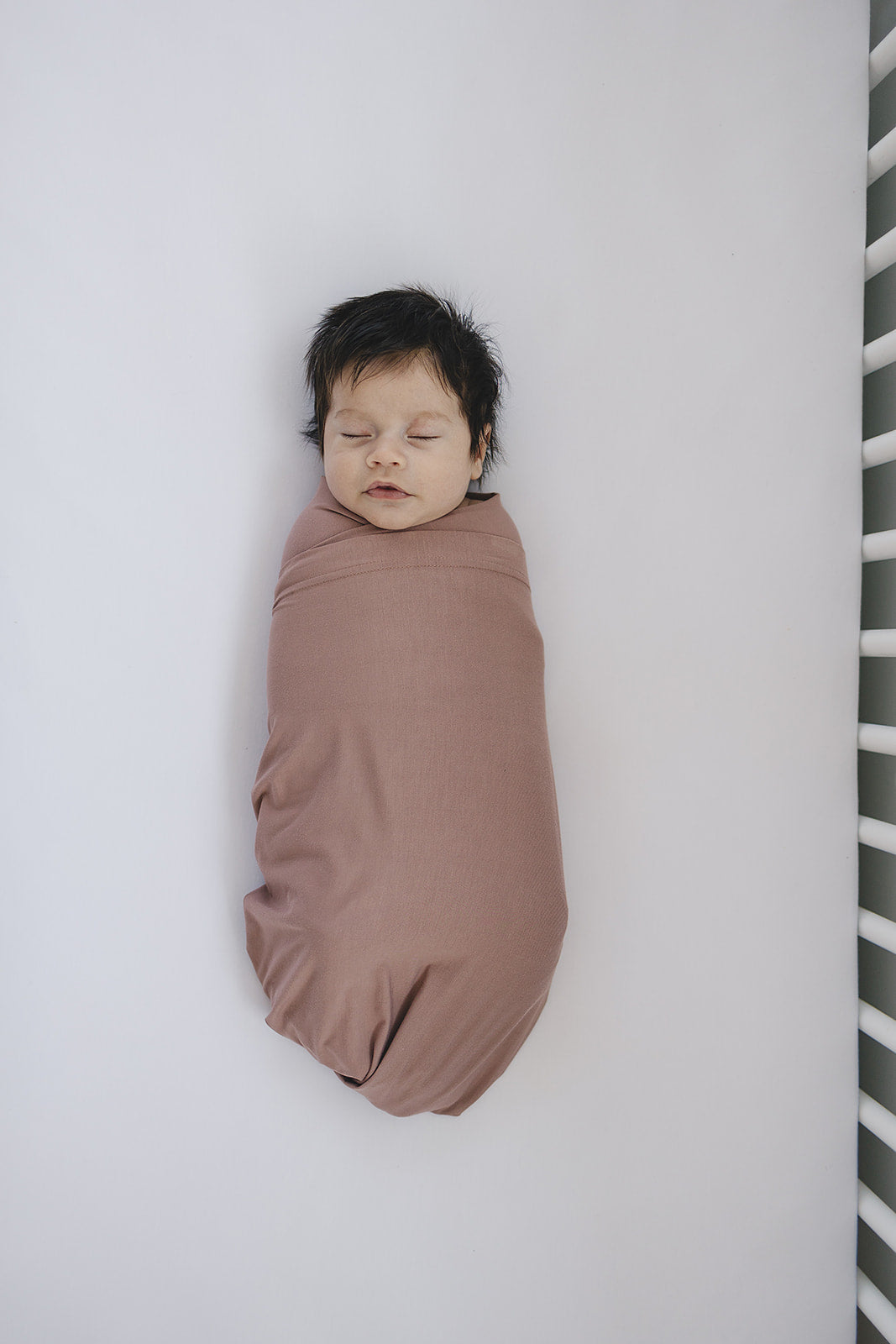 Infant swaddled in Bamboo Stretch Swaddle Dusty Rose, showcasing its soft, breathable fabric and peaceful sleeping position.