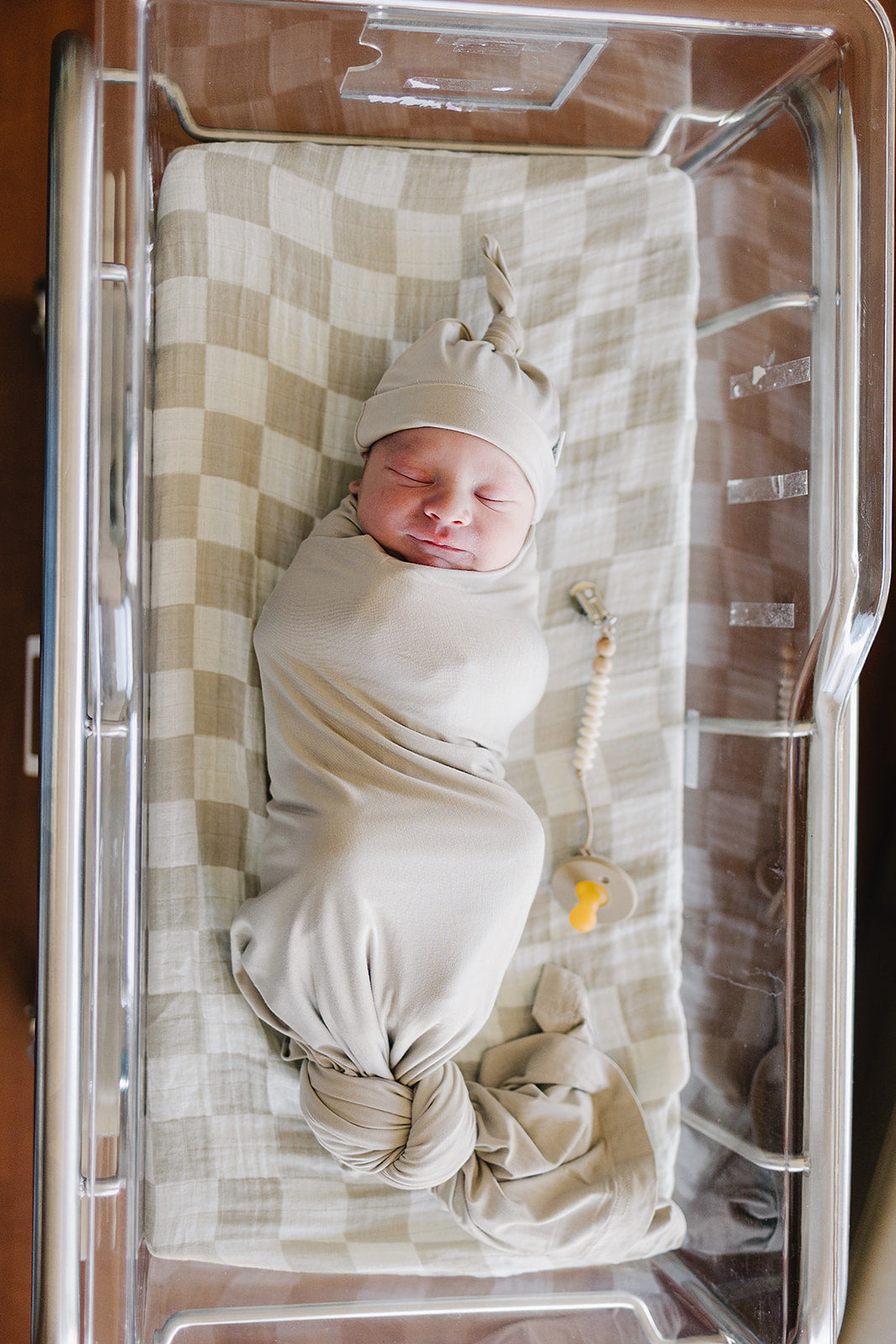 Bamboo Stretch Swaddle Oatmeal wrapping a newborn in a bassinet, showcasing neutral, soft fabric.