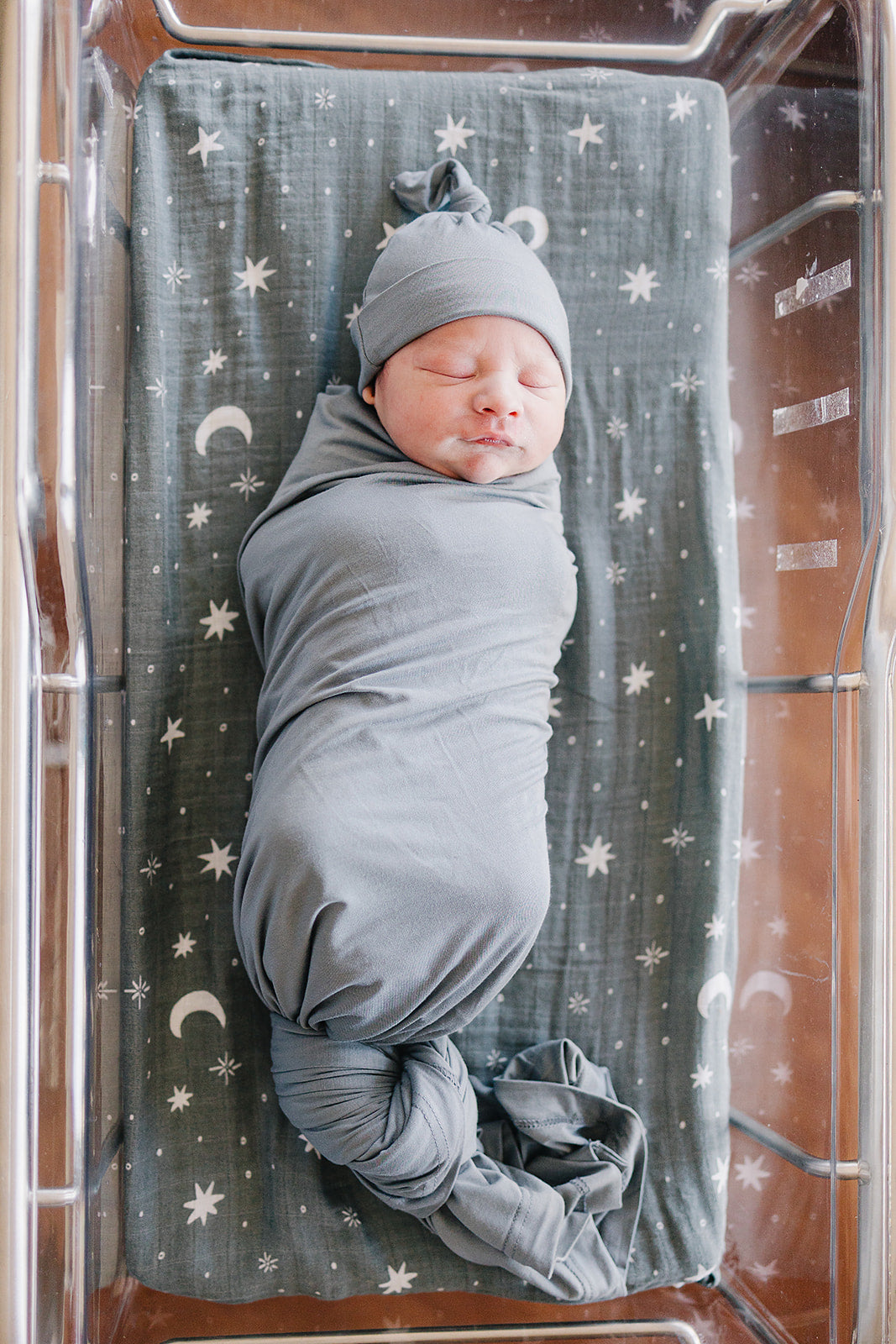 Bamboo Stretch Swaddle Dusty Blue wrapping a newborn in a cozy hospital bassinet setting.