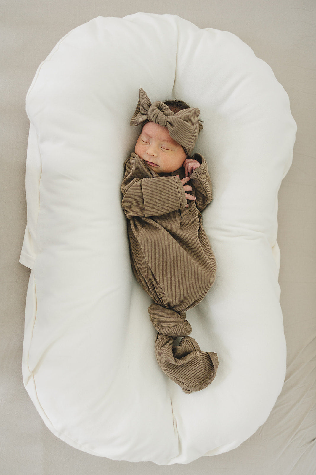 Newborn in a cocoa organic cotton ribbed head wrap and matching outfit, peacefully resting on a soft, plush surface.
