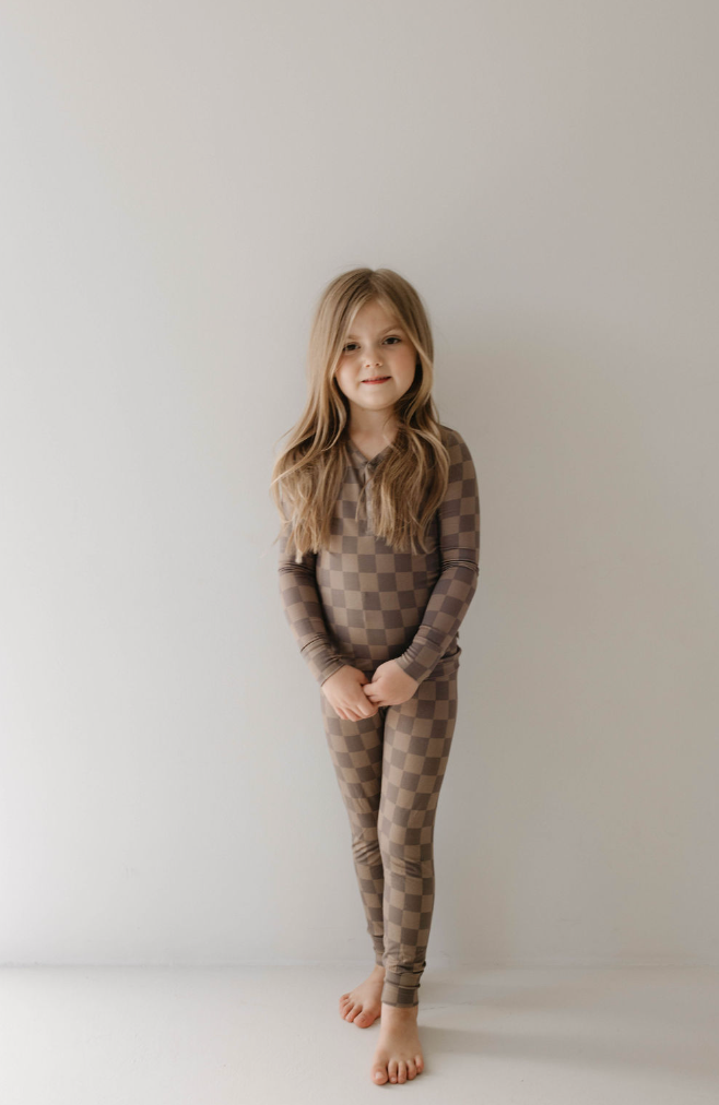Child in faded brown checkerboard bamboo pajamas, featuring a long-sleeve top and elastic waist pants.