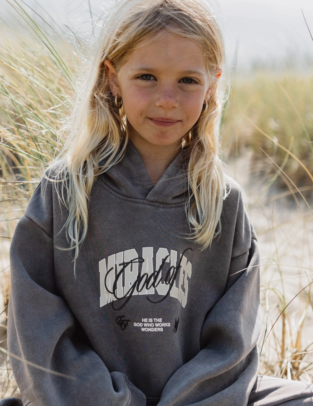 Smiling child in God of Miracles kids hoodie, featuring stylish embroidery and soft oversized fit, perfect for play.