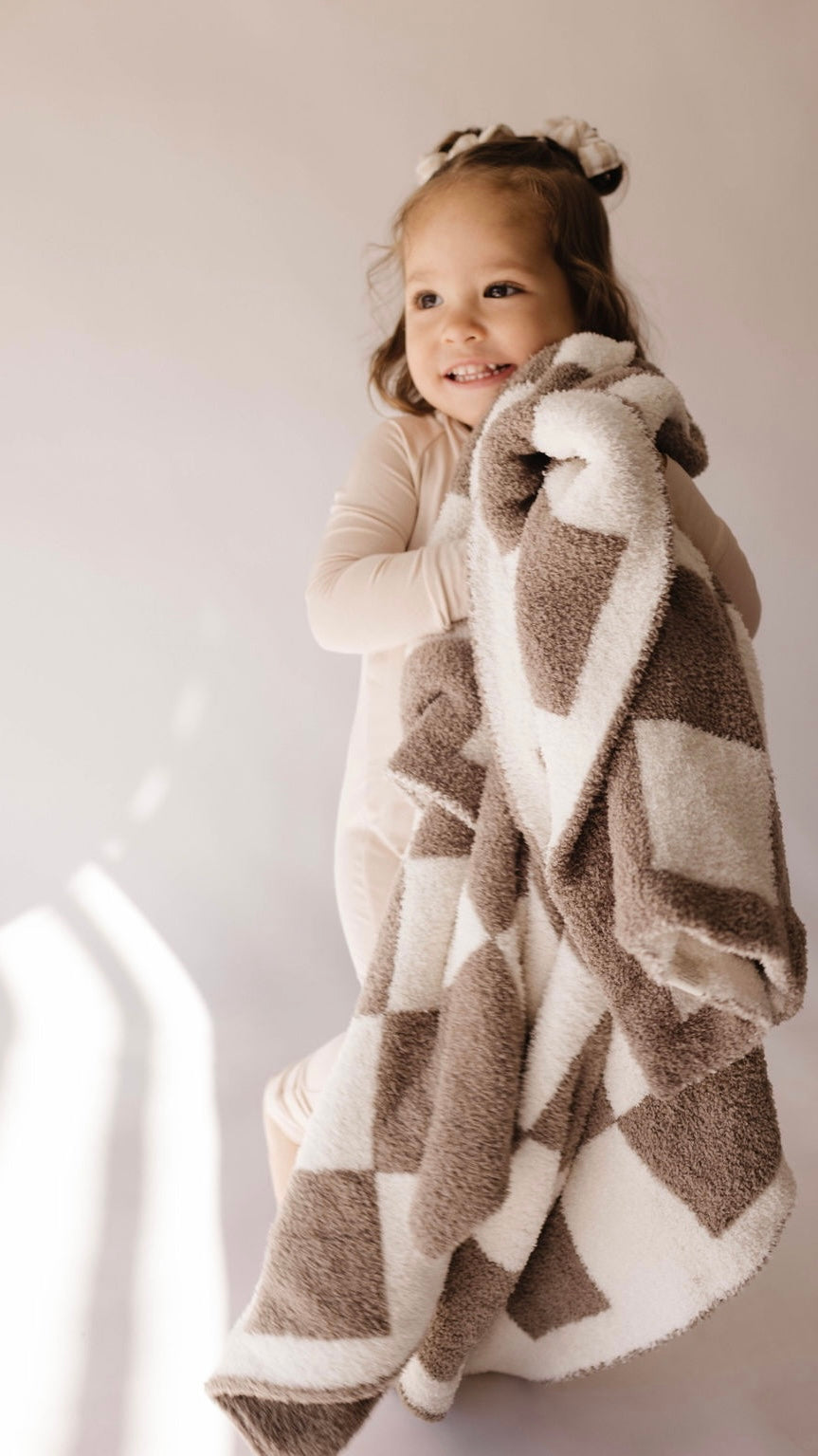 Smiling child holding a cozy mushroom checkerboard plush blanket, perfect for whimsical nursery decor.