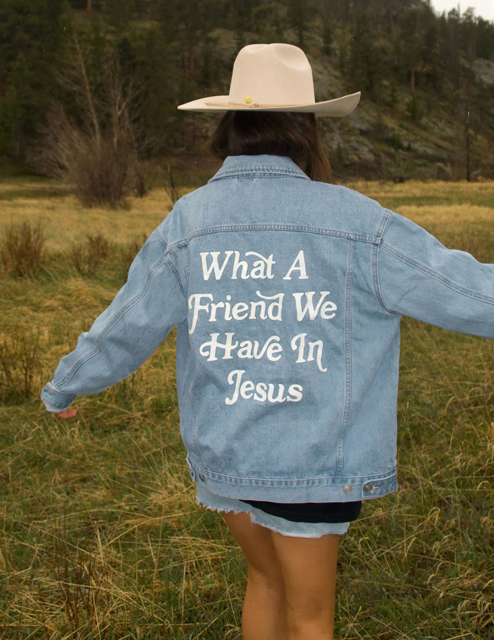 Woman wearing a What a Friend in Jesus Denim Jacket in a scenic outdoor setting.