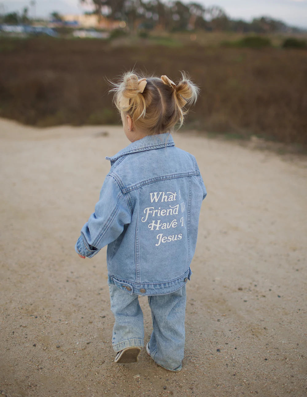 Child wearing What a Friend in Jesus kids denim jacket on a path, showcasing its stylish design and meaningful message.