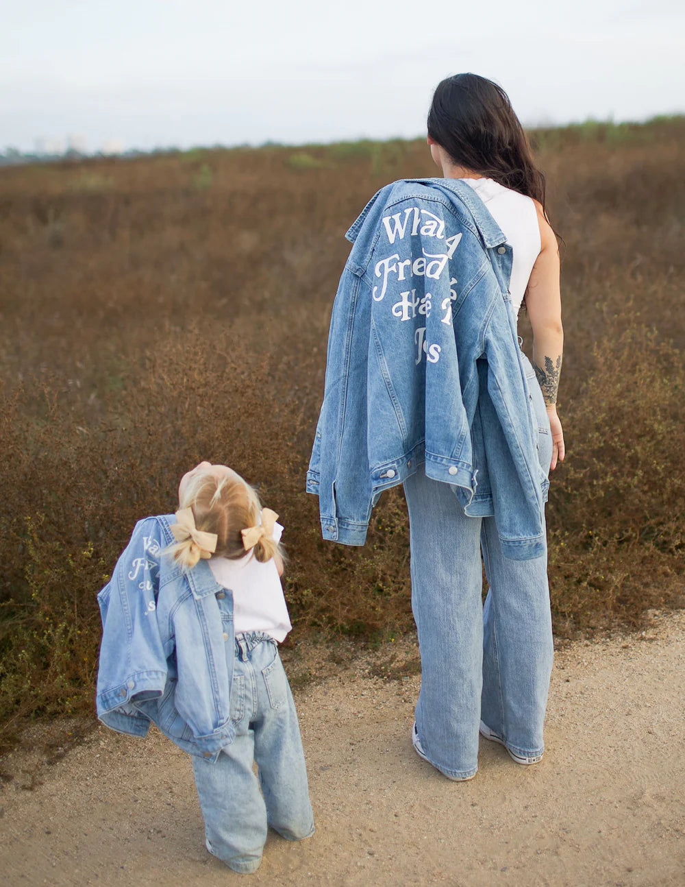 Mother and child wearing matching What a Friend in Jesus kids denim jackets in a natural outdoor setting.